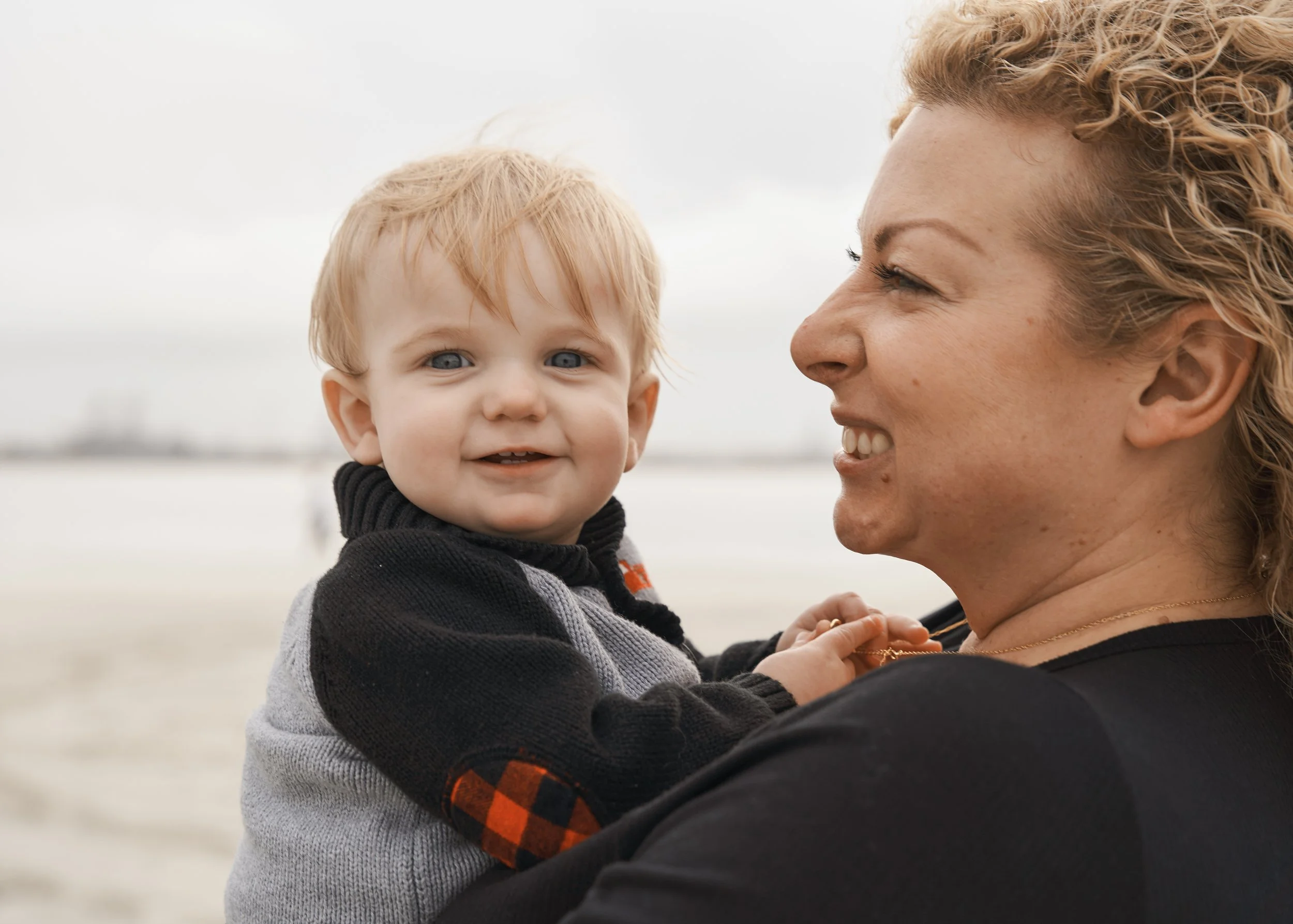 A woman holding a young child with a blurred beach background.