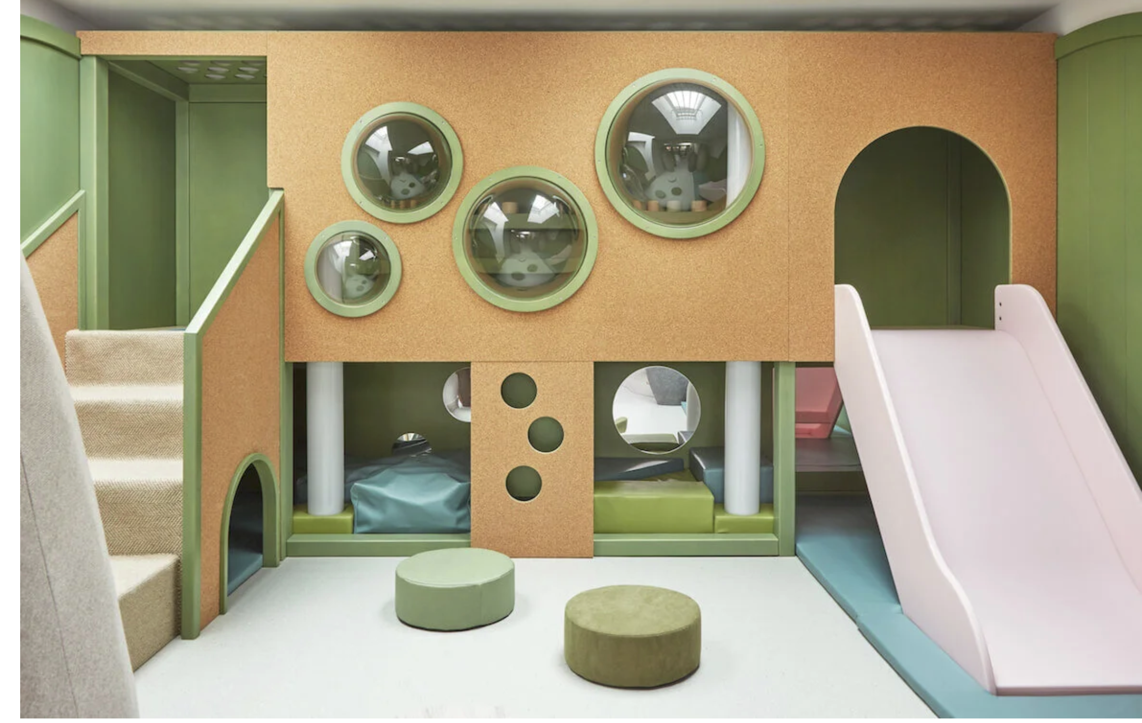 Colorful indoor play structure resembling a house with a slide, multiple circular windows, and soft cushioned flooring, designed for children.