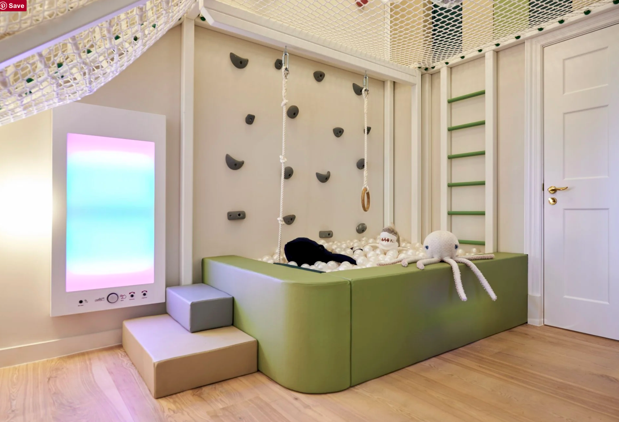 Indoor play area with a ball pit, climbing wall, and gymnastic rings, featuring plush toys and a colorful wall panel.