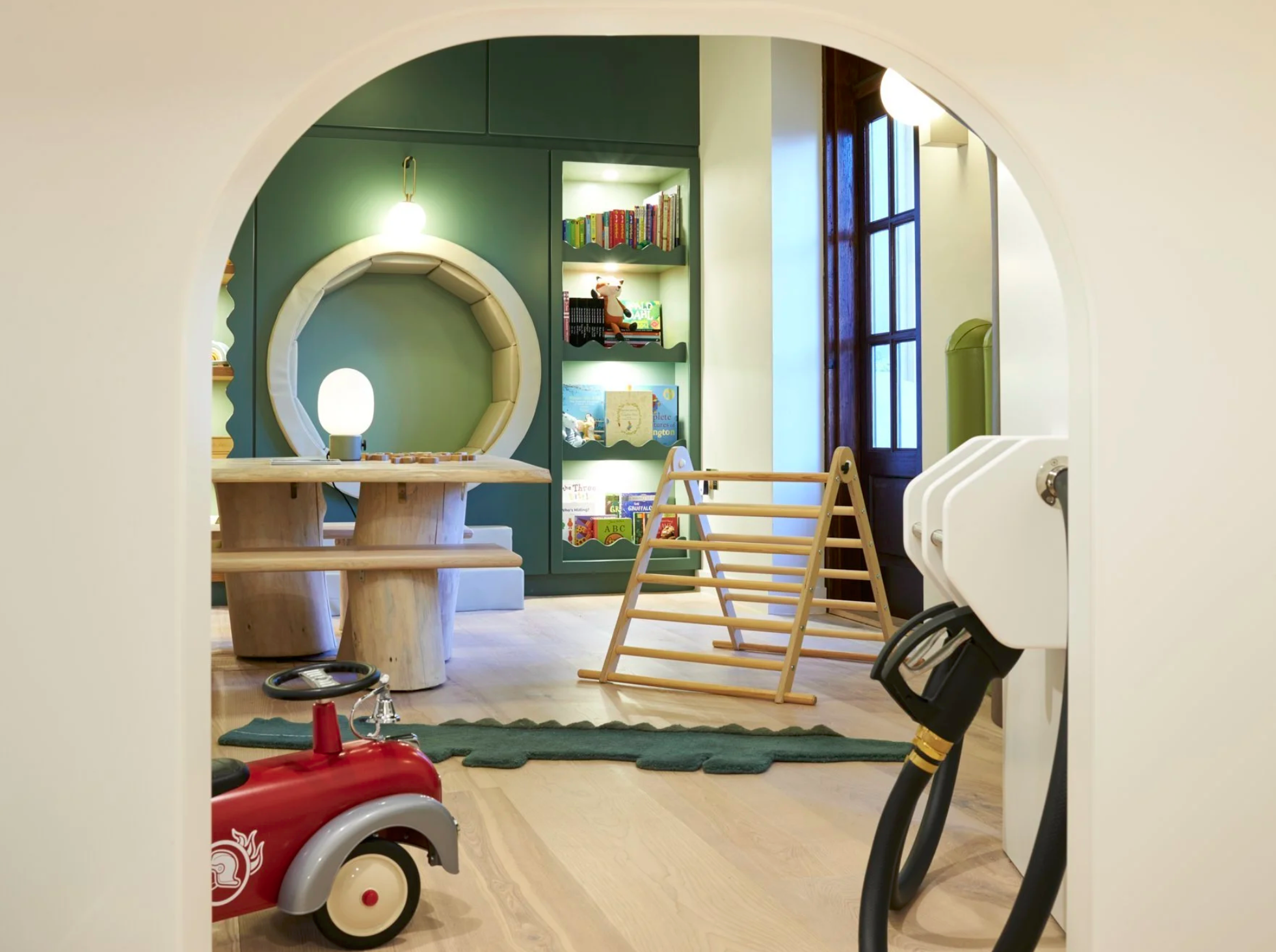 Children's playroom with wooden climbing frame, bookshelves, and toys, viewed through an arched doorway.