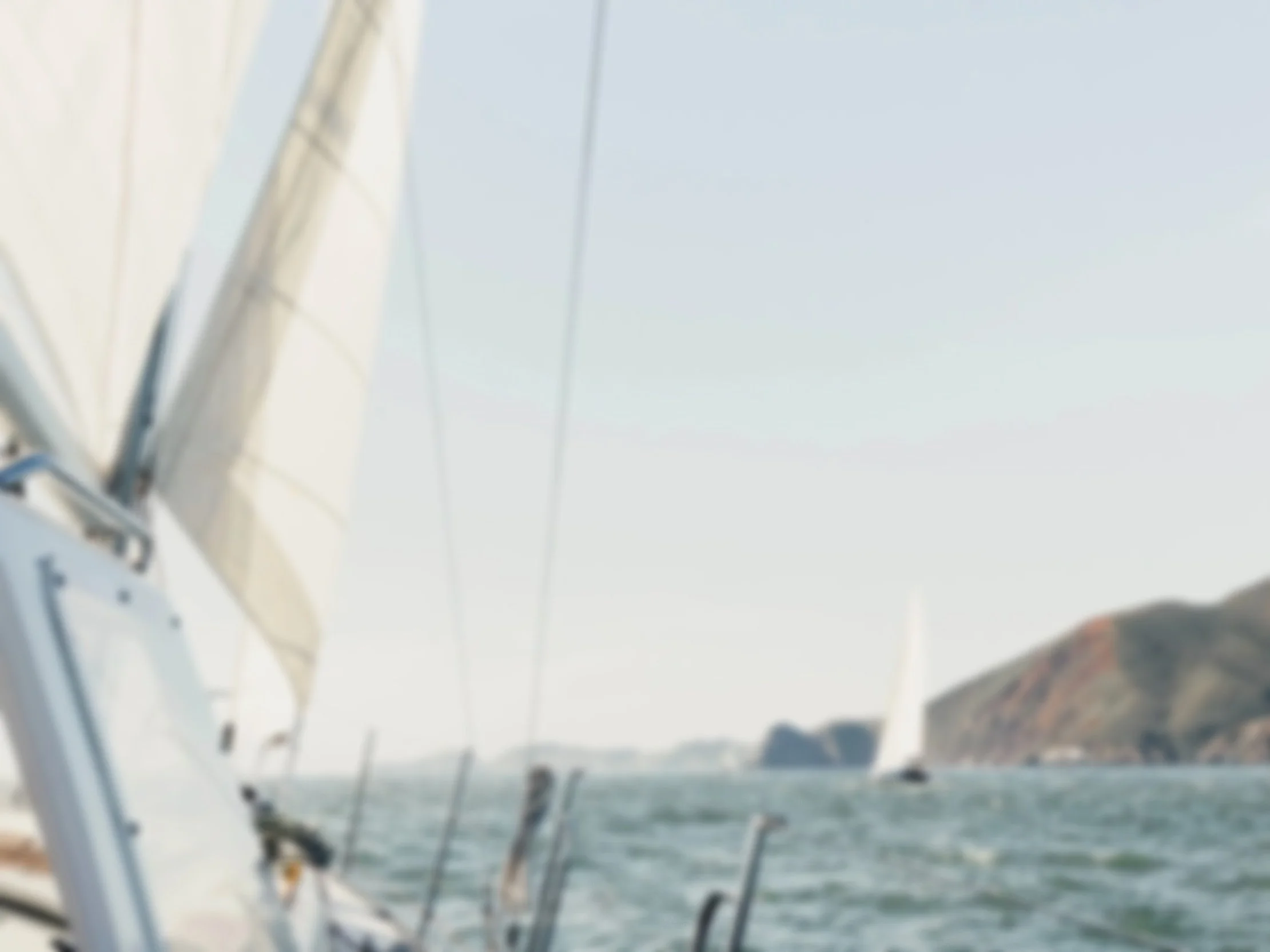 Blurry photo of sailboats on the water near a coast with hills in the background.