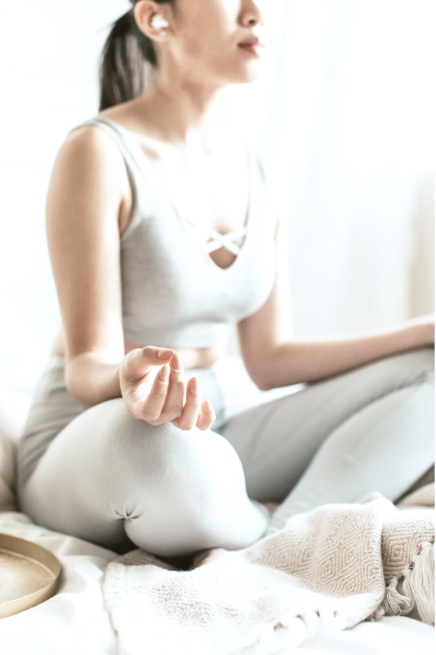 Woman practicing meditation in a peaceful, well-lit room, sitting cross-legged with eyes closed and hand resting on her knee.