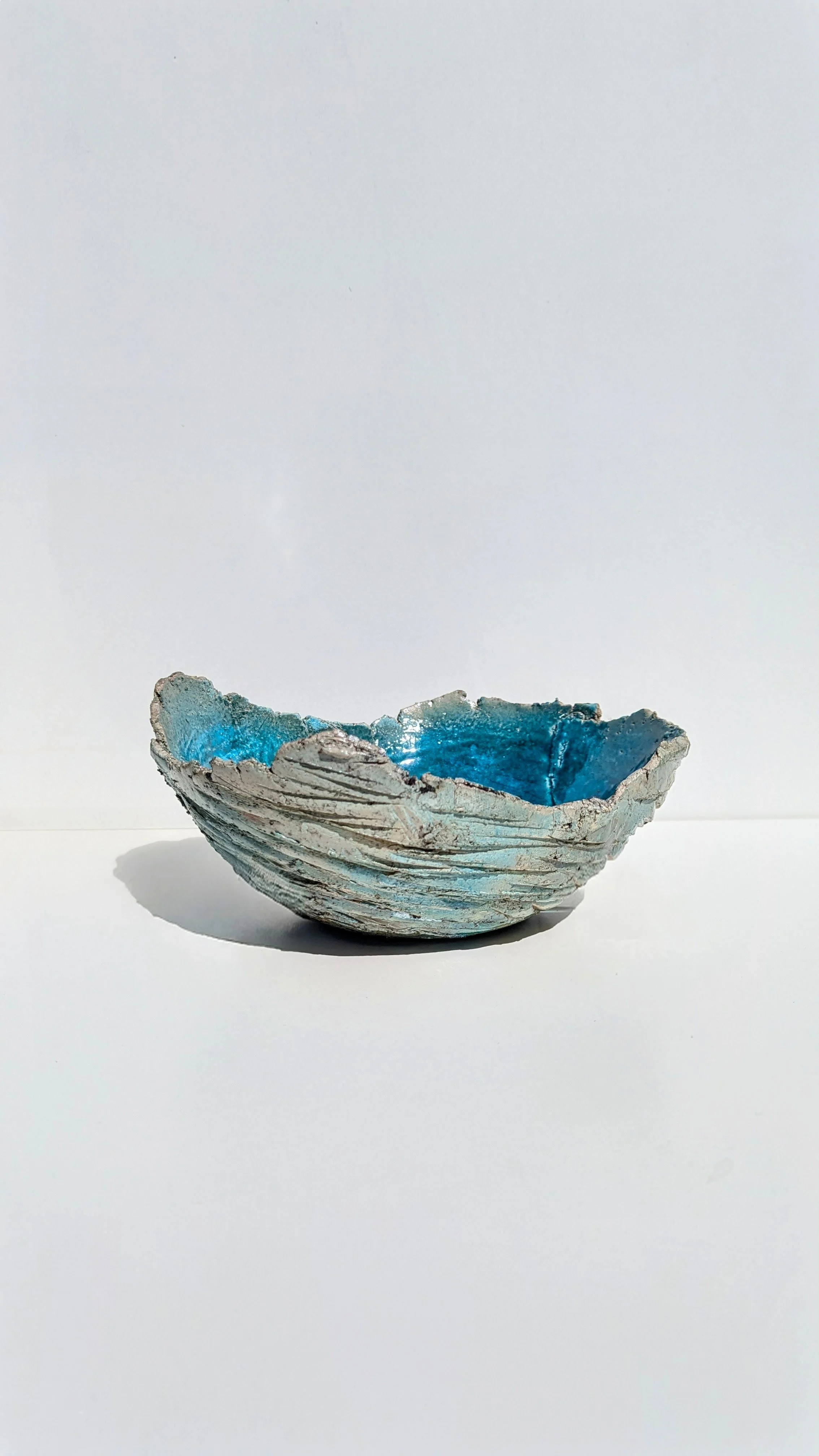 A textured ceramic bowl with a blue glaze interior, placed on a white surface with a plain white background.