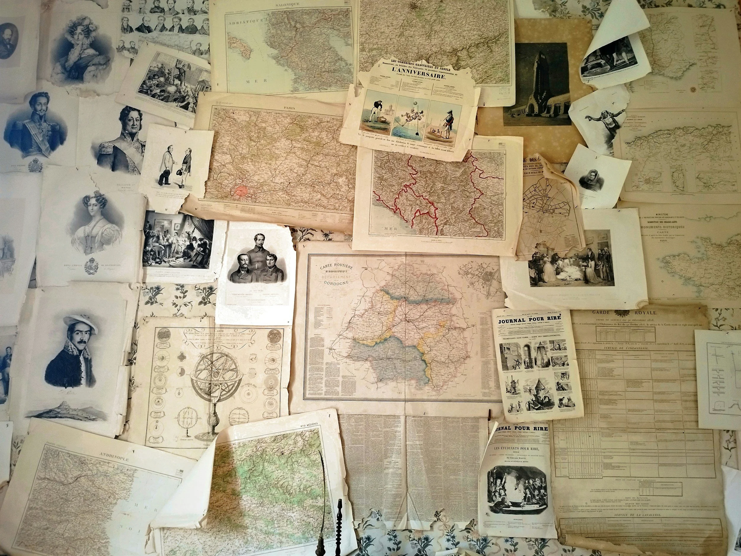 A collection of vintage maps, sketches, and old documents spread across a surface, including portraits, newspapers, and handwritten notes.