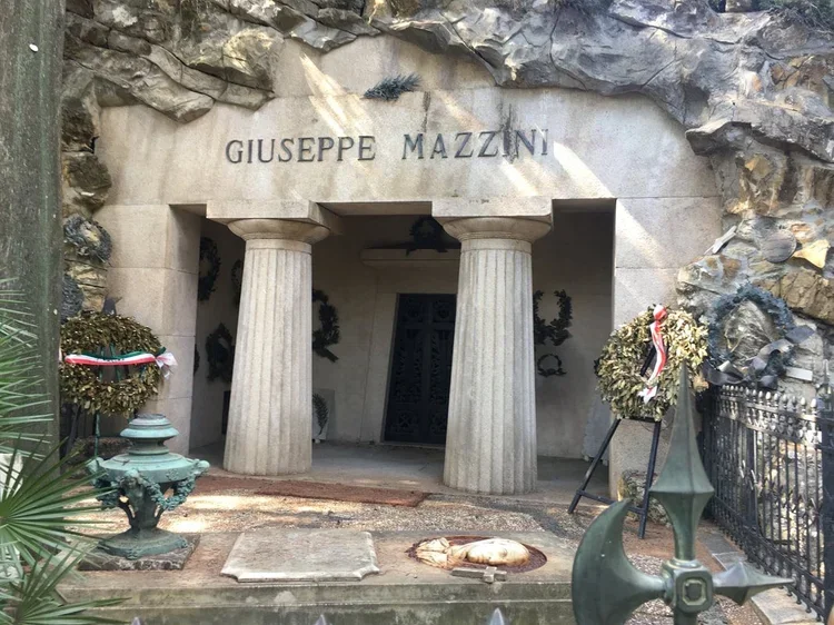 Memorial with the name Giuseppe Mazzini, flanked by two large columns, with wreaths on either side and surrounded by a rocky cave-like structure.