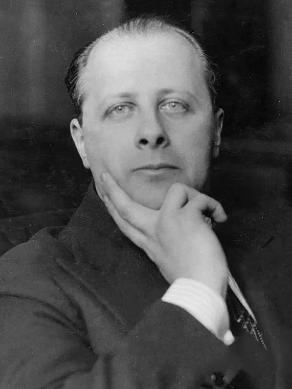 Black and white portrait of Carlo Rosselli in a suit with slicked-back hair, resting his chin on his hand in a thoughtful pose.