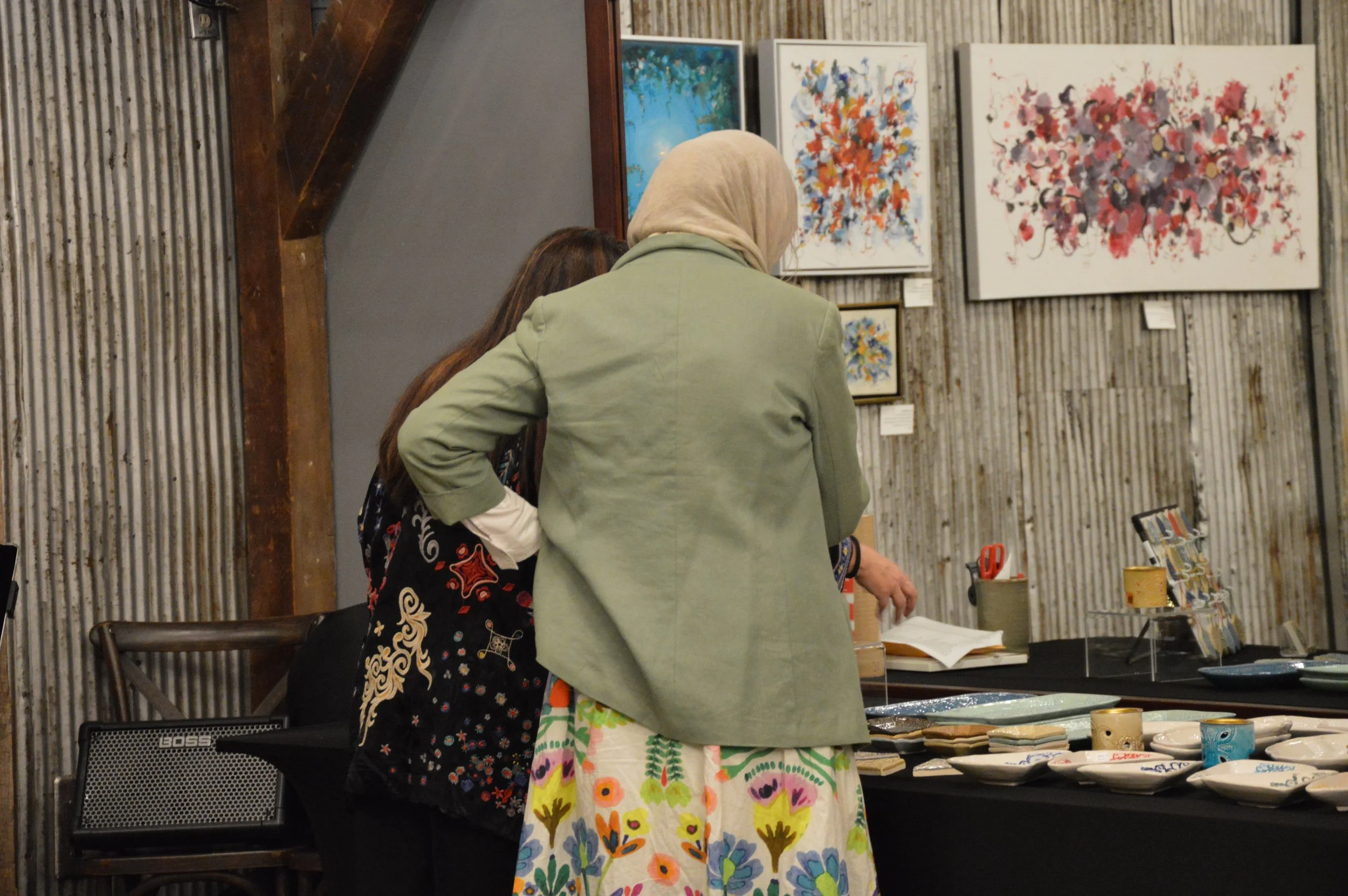 Egyptian visual artist Afaf Khalil standing behind Kuwaiti ceramist Najla Alradwan, examining tiles and ceramics at the Middle Eastern Arts Collective Inaugural Art Gallery