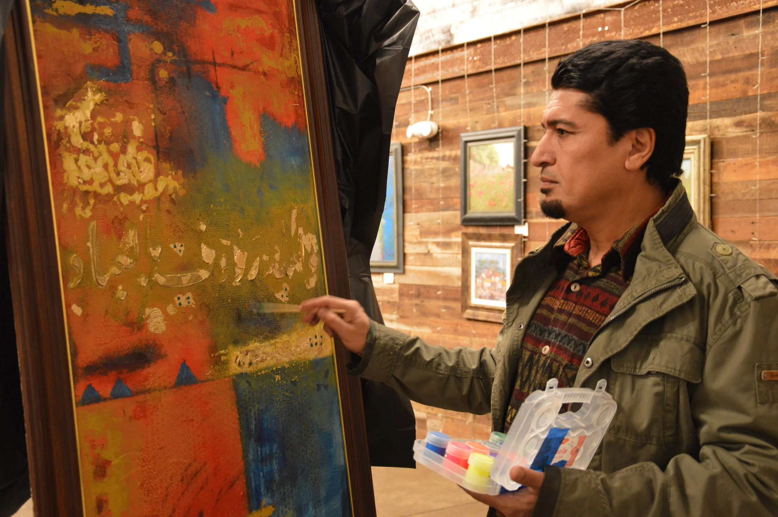 Iraqi artist Ahmed Alkarkhi live painting at Middle Eastern Arts Collective inaugural art gallery in Alexandria, Virginia. Painting consists of blue, orange, and gold paint with arabic letters in the center.