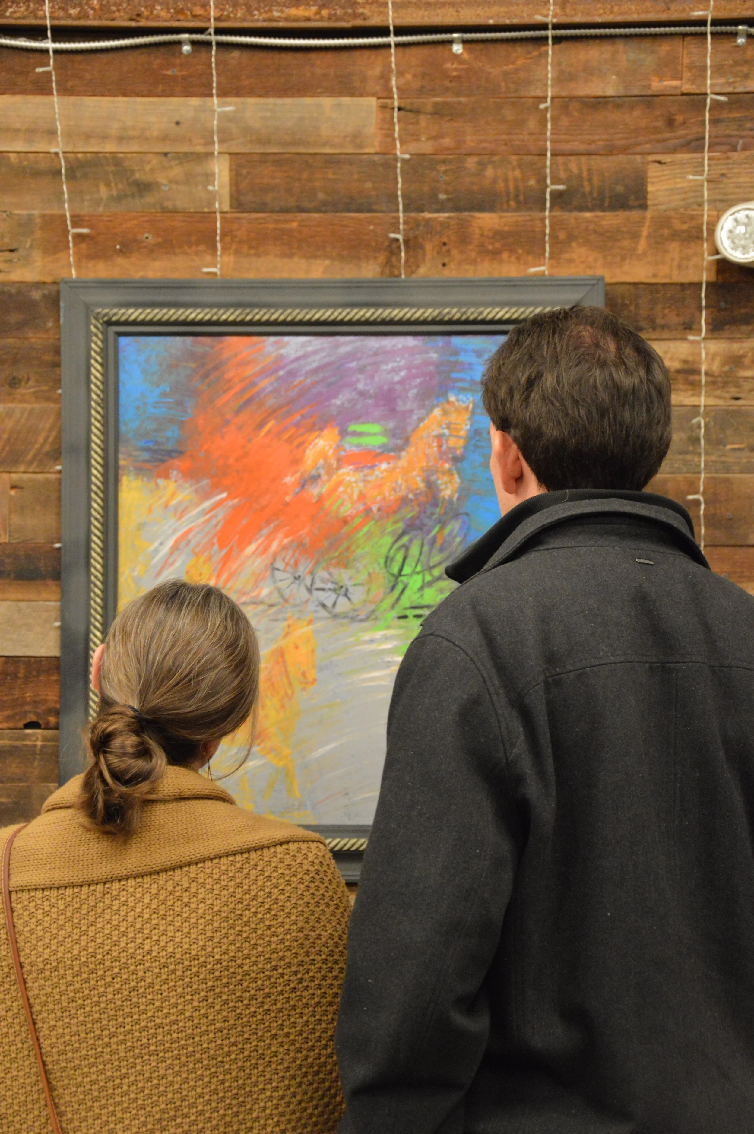 Two attendees of the Middle Eastern Arts Collective's inaugural art gallery standing next to each other in front of a painting by Iraqi visual artist Ahmed Alkarkhi