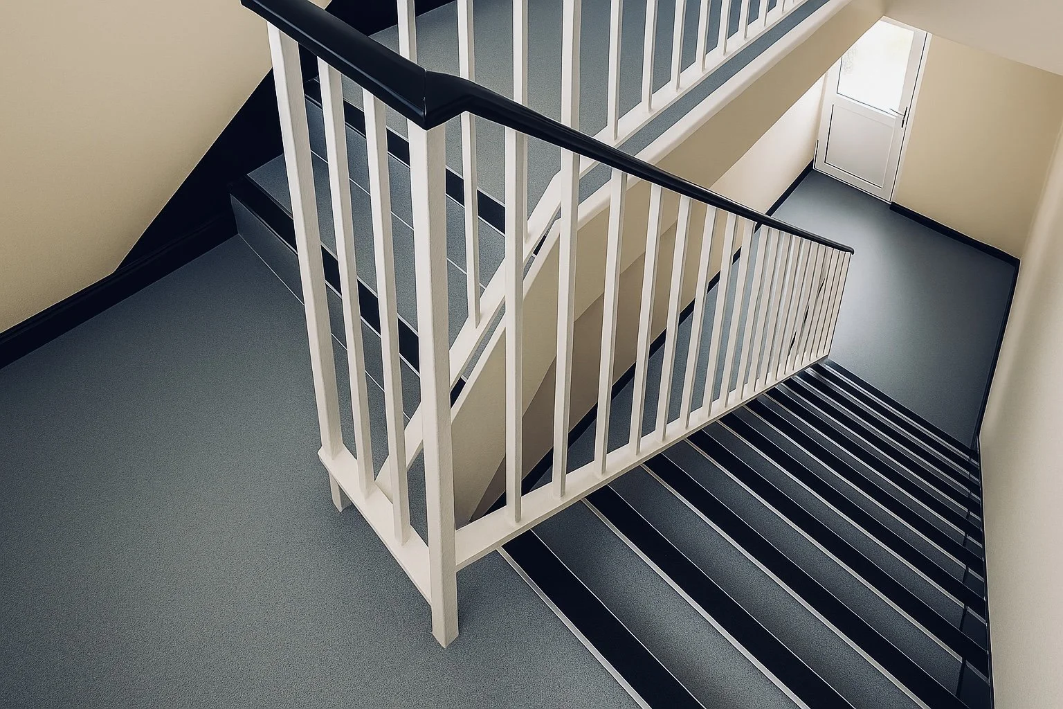 Indoor staircase with black handrails, blue carpeted steps, white walls, and a corner landing.