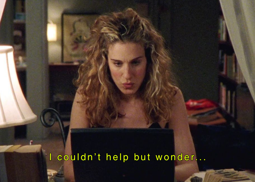 A woman with curly, blonde hair looking at a laptop with a contemplative expression.