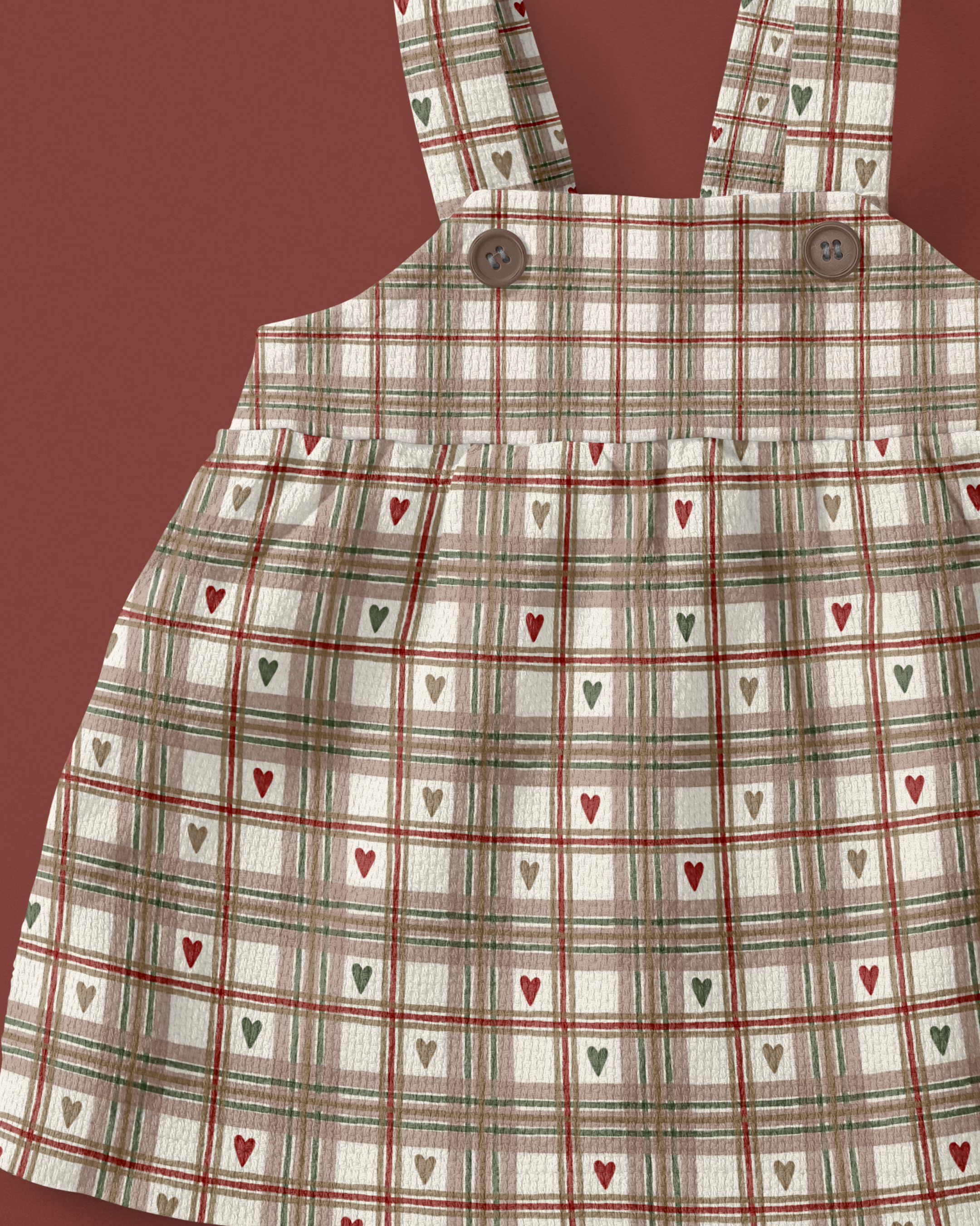 A plaid dress with heart patterns and buttons on shoulder straps, set against a reddish background.