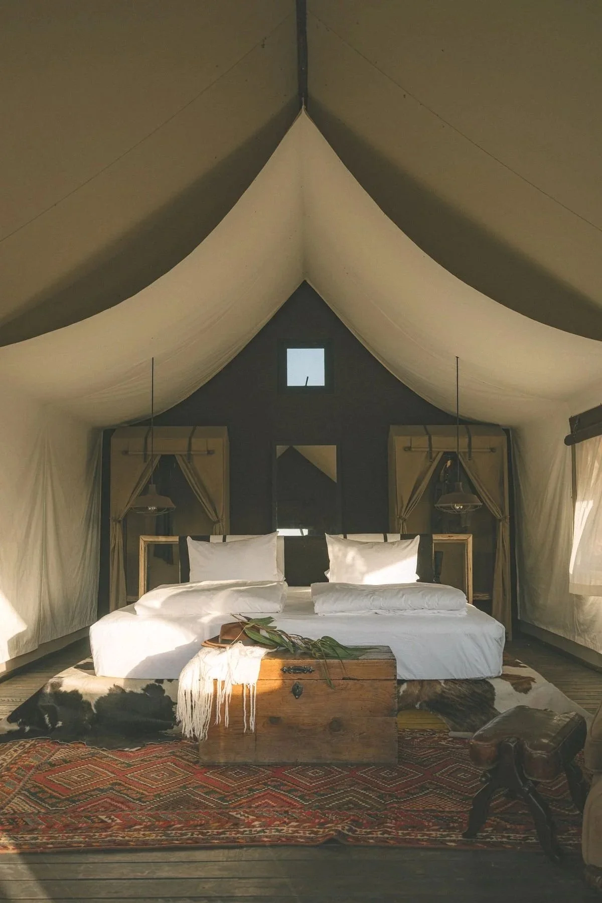 Cozy bedroom inside a tent with a bed, pillows, a wooden chest at the foot of the bed, and a patterned rug on the wooden floor.
