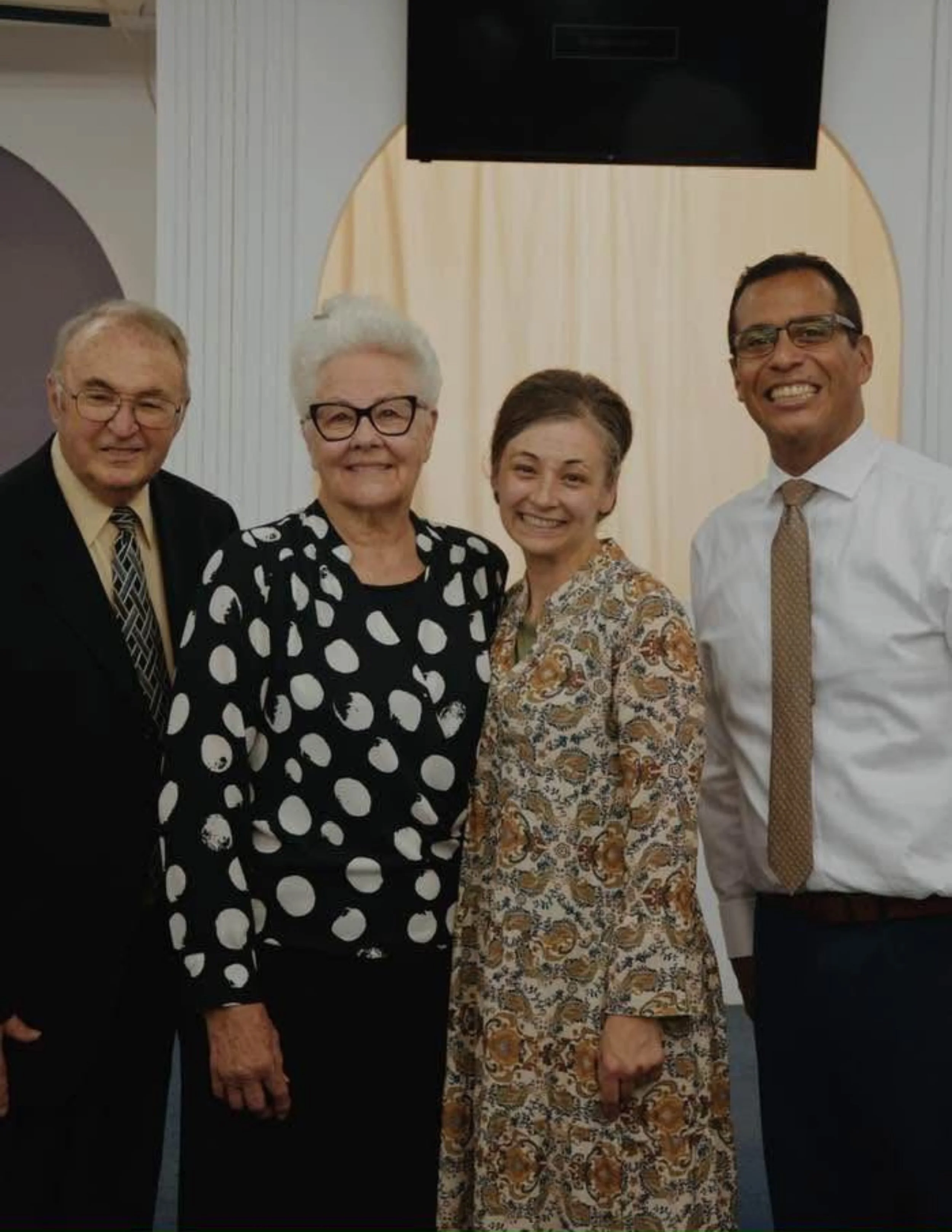 Group of five people standing together indoors, smiling for a photo.