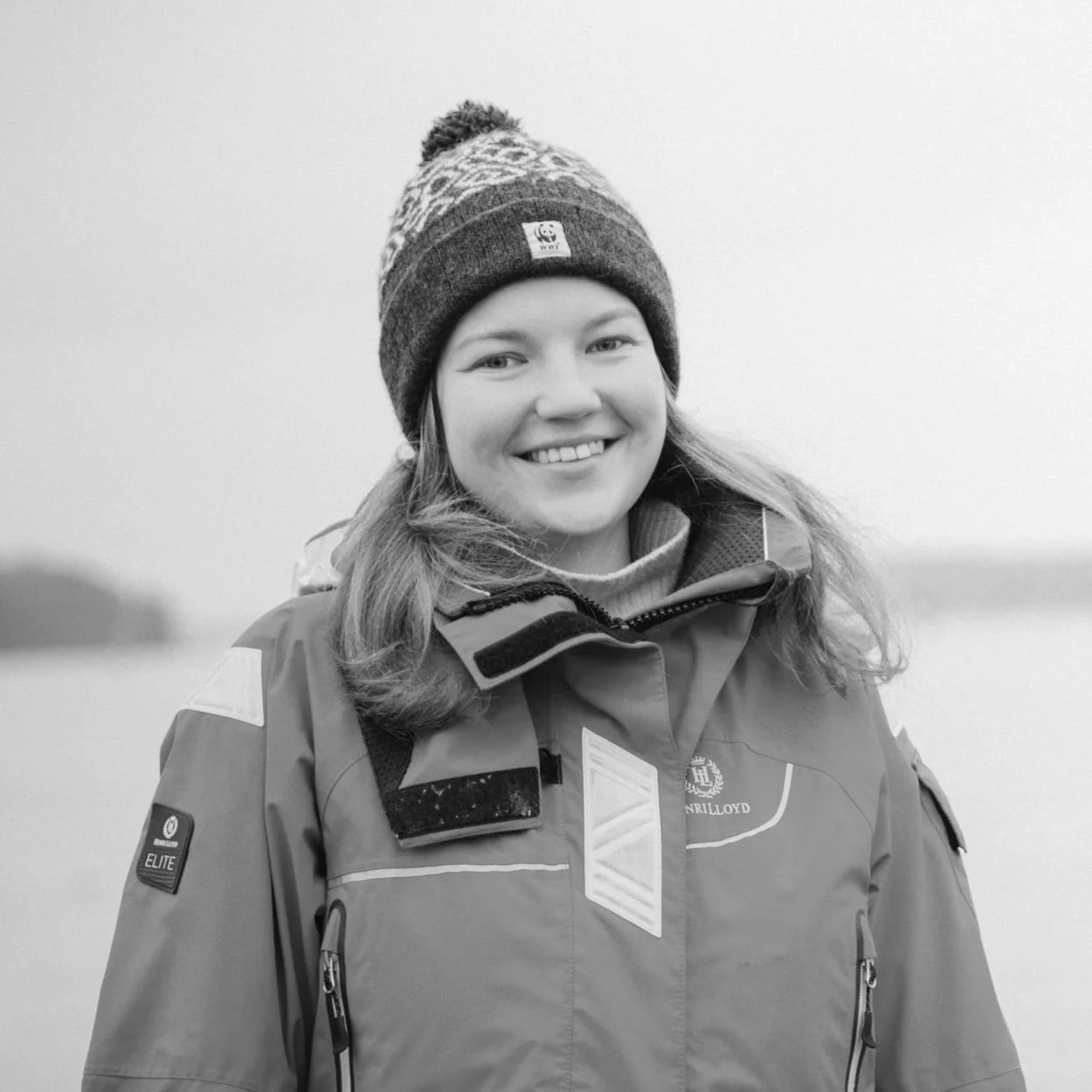 Black and white photo of a smiling woman with long hair, wearing a sweater and outdoors.