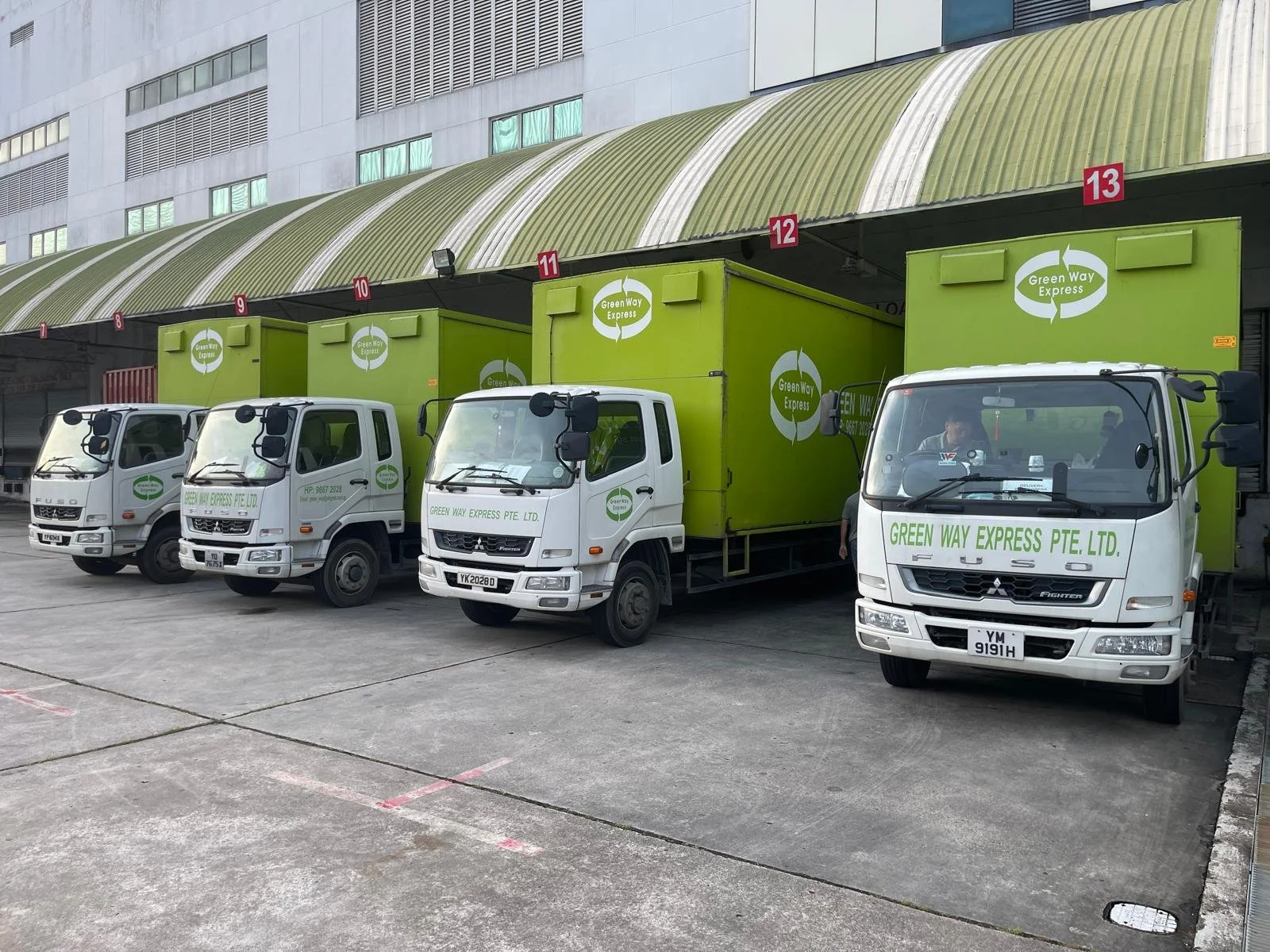 Four green and white delivery trucks labeled "Green Way Express" parked in a loading dock area.
