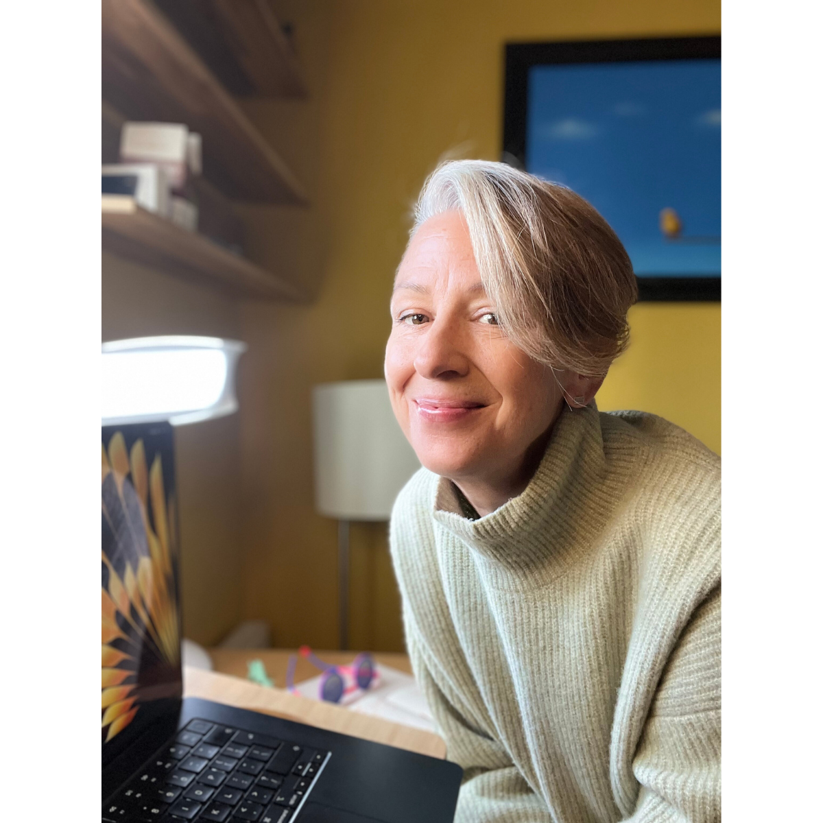 White woman sat at her desk smiling at the camera.