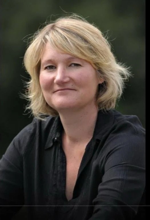 A woman with blonde hair and a black shirt smiling outdoors.