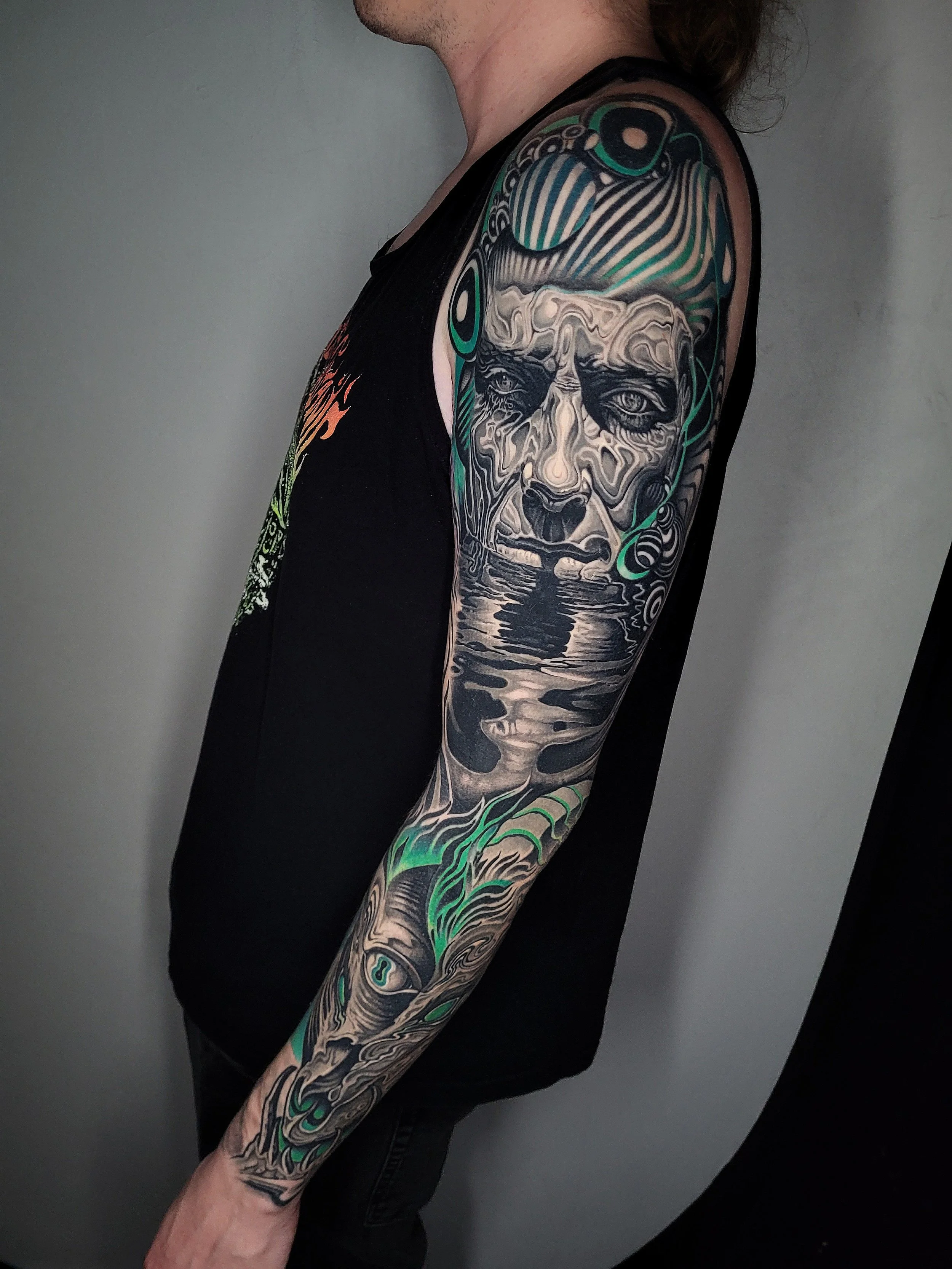 Tattoo of a man's face with water reflections and abstract designs on the arm.