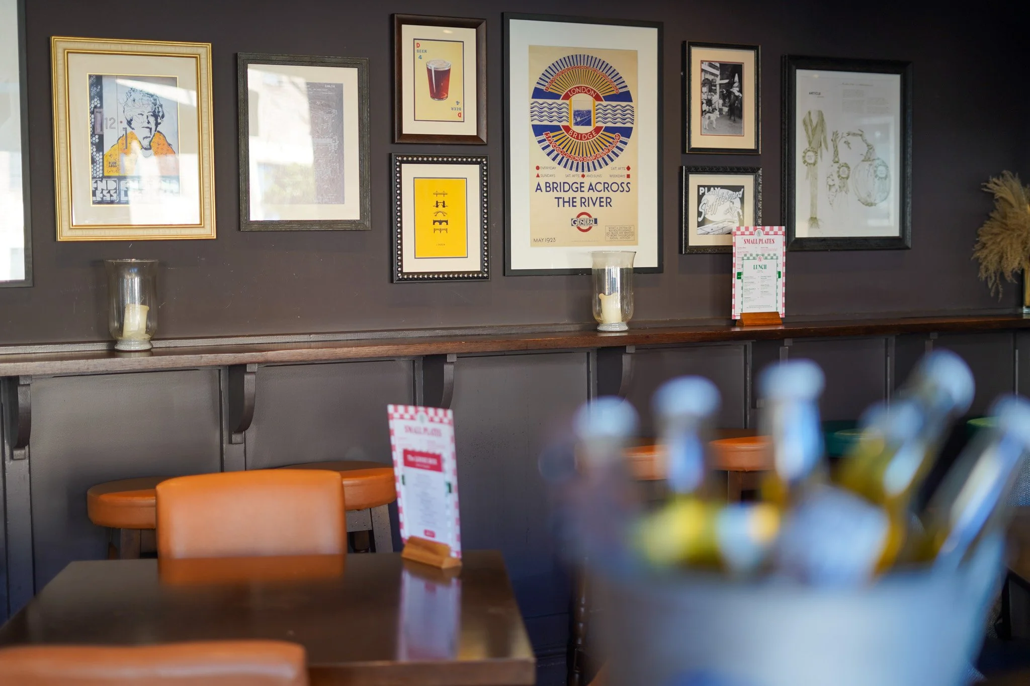 Interior of a restaurant with wall decor, including framed artwork, posters, candles, and tables with menu cards and bottles.