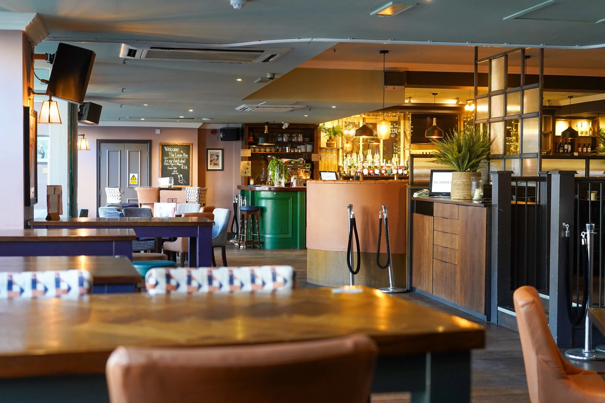 Empty pub-style bar and seating area with tables, chairs, and a bar counter illuminated by warm lighting.