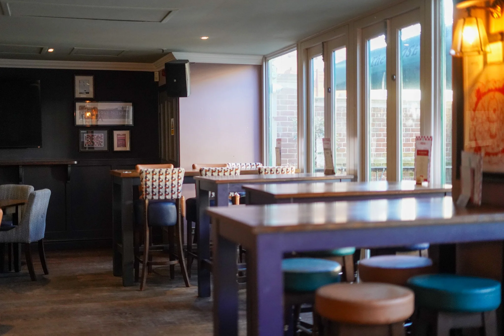 Empty restaurant or café interior with wooden tables, colorful stools, and large windows letting in natural light.