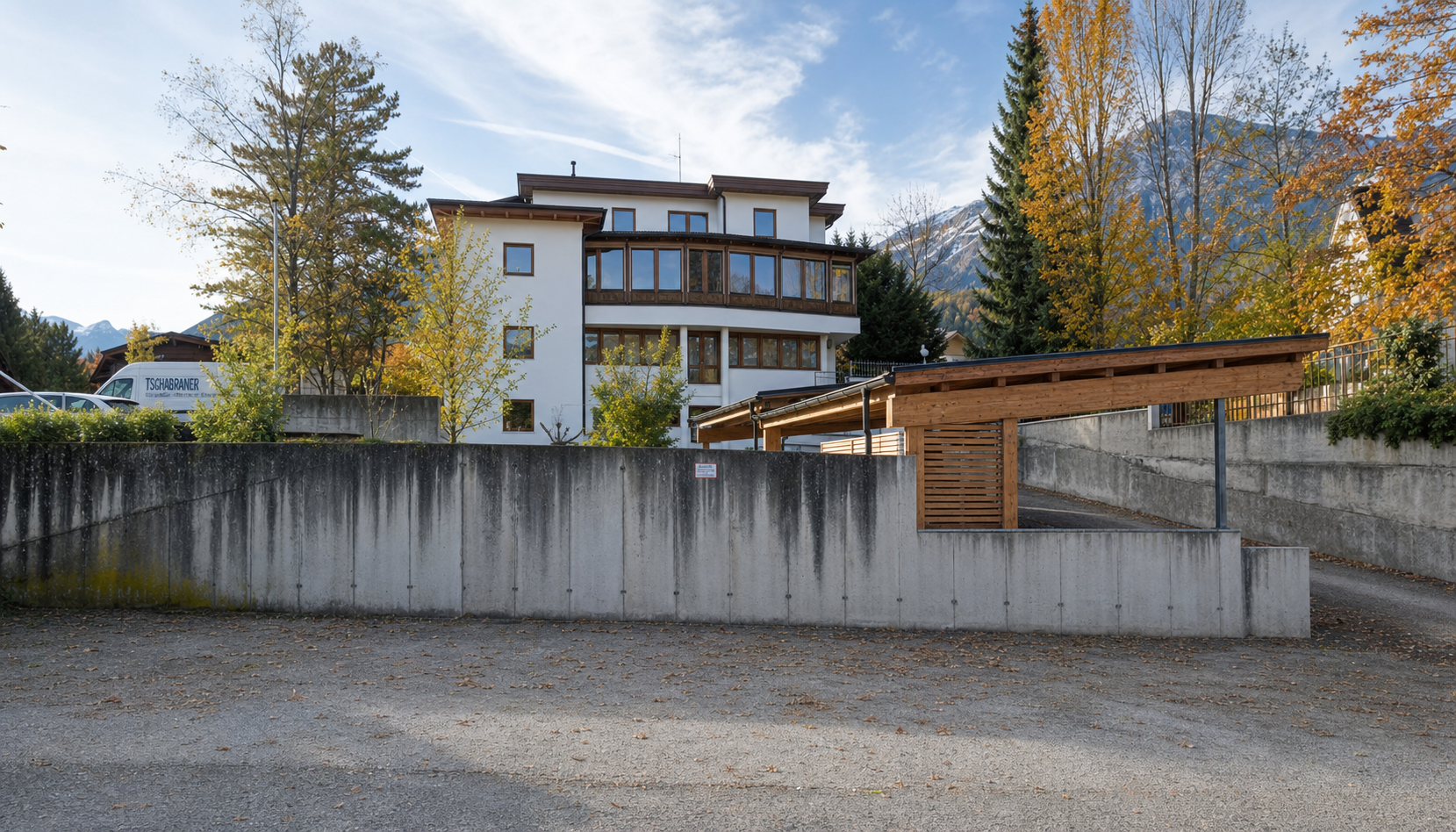 Mehrstöckiges Haus mit großen Fenstern, umgeben von Bäumen mit Herbstlaub, im Gebirge.