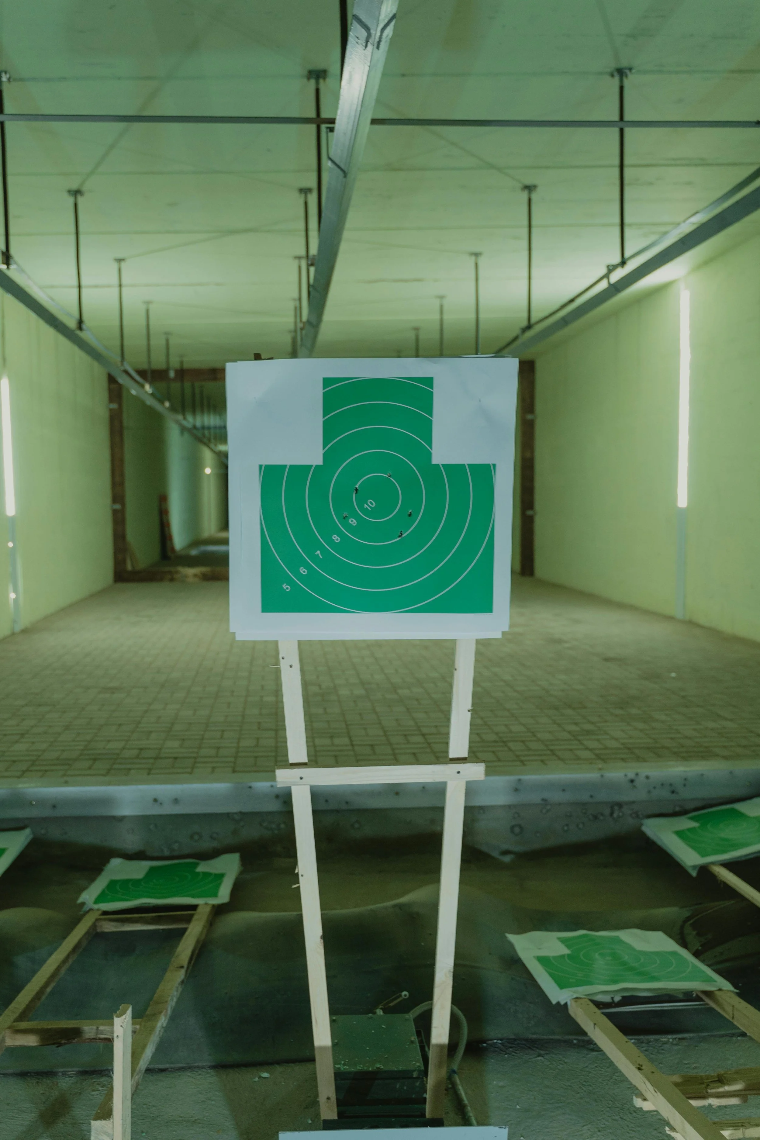 Indoor shooting range with green paper target on stand, surrounded by additional targets on the ground.