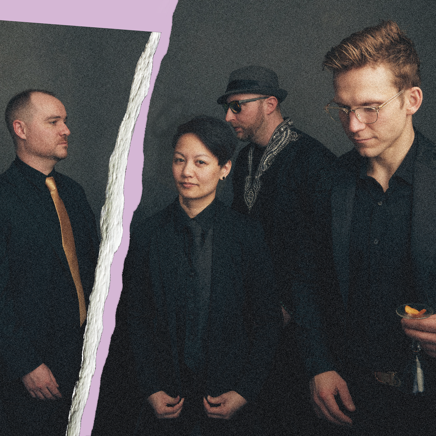A man with curly dark hair and glasses playing an electric guitar at an indoor event or convention, with booths and banners in the background.