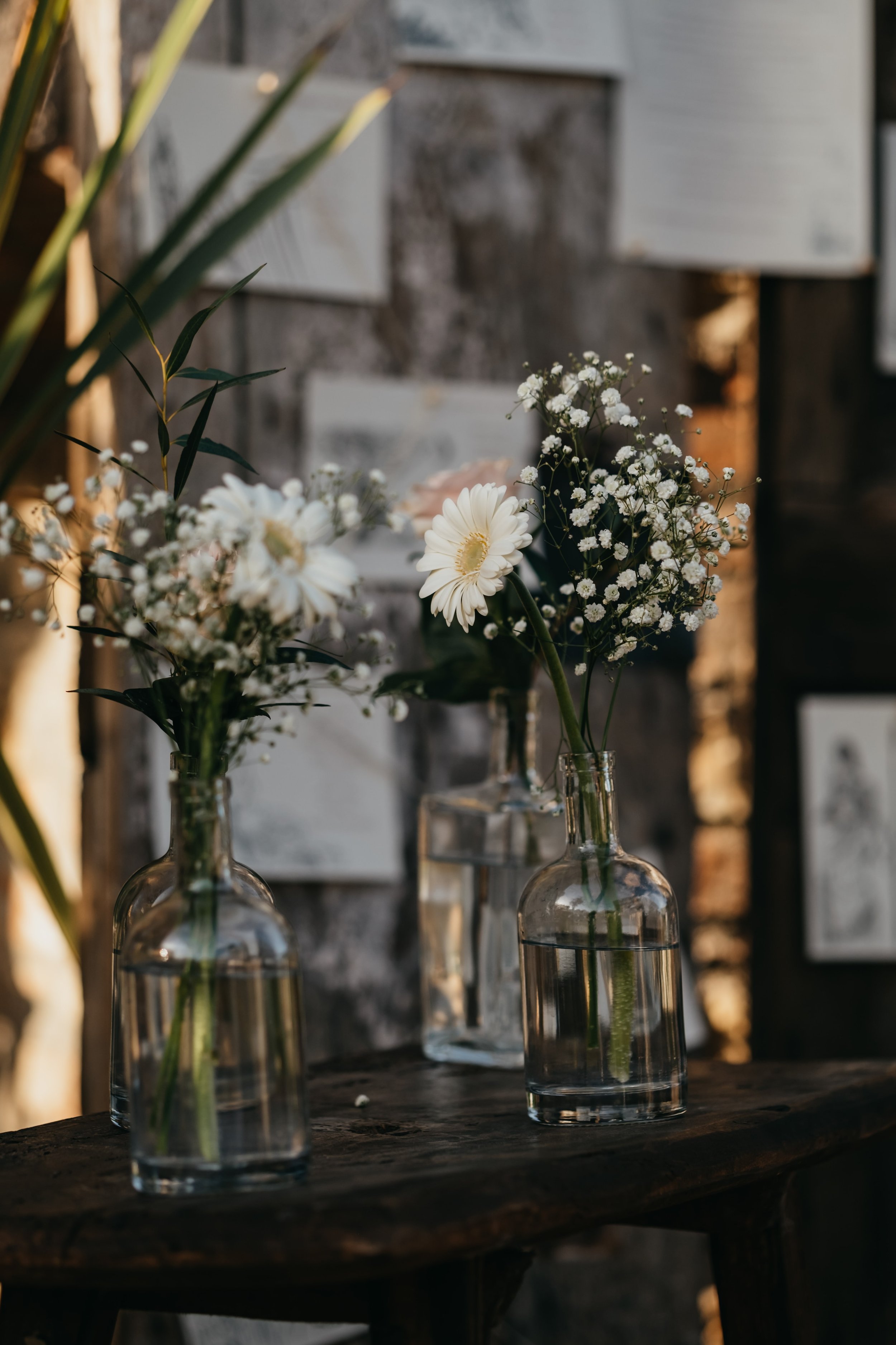 Three glass vases with white flowers, including daisies and baby's breath, placed on a wooden surface.