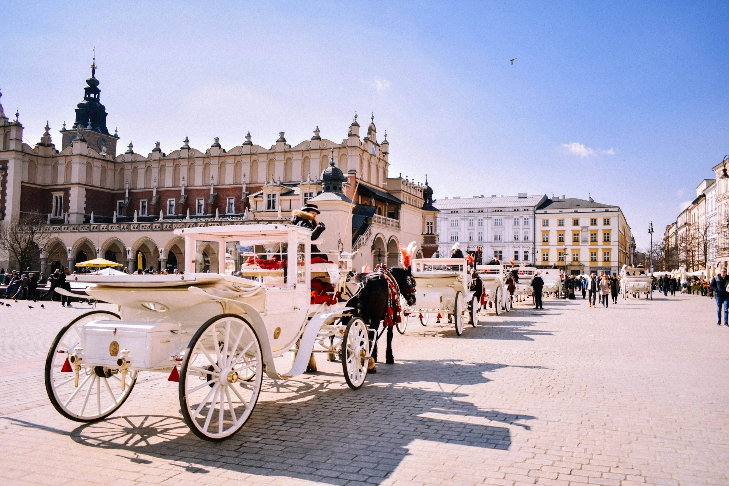Horse-drawn carriages lined up on a city square with historic buildings and a clear sky.