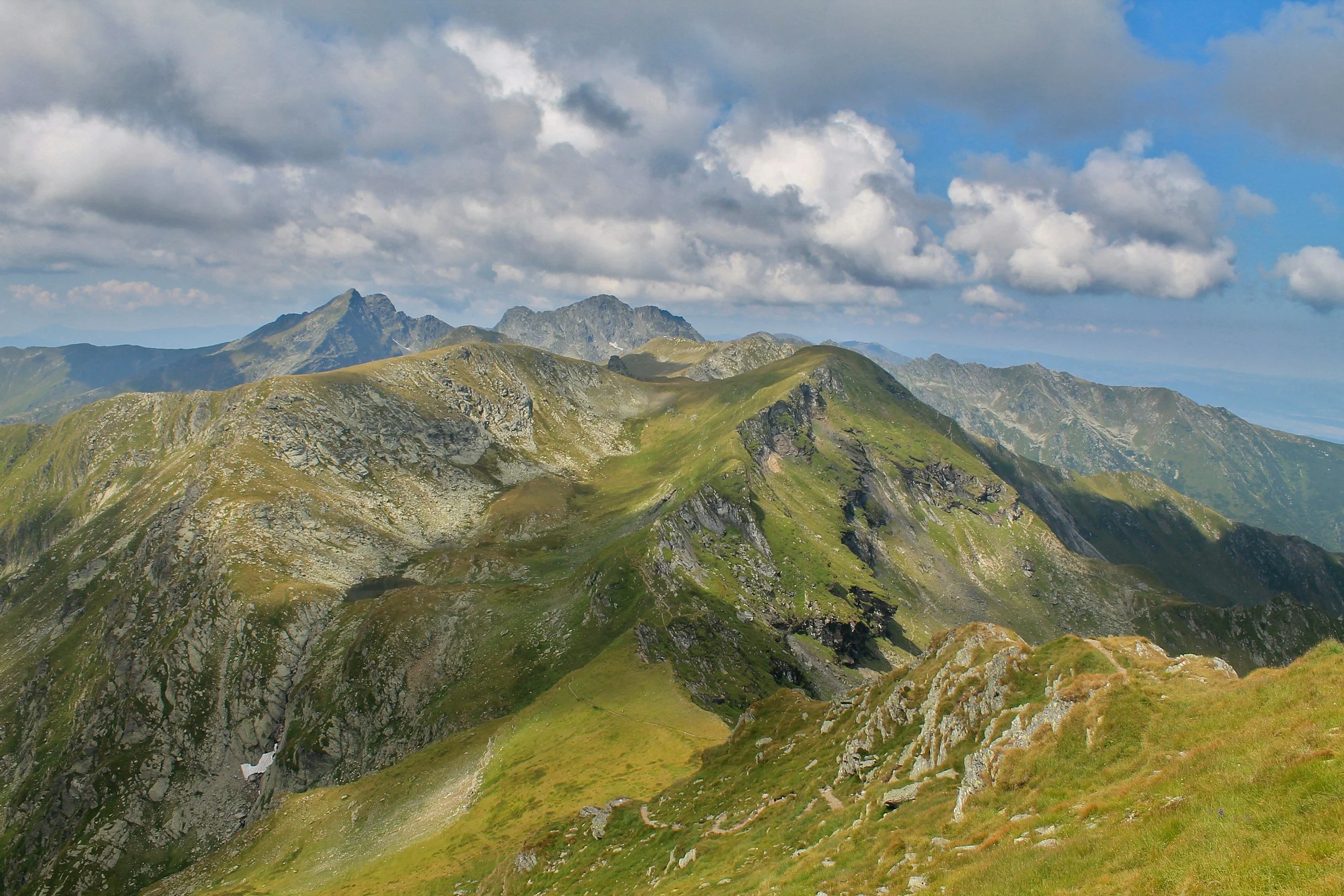 Scenic view of green mountain peaks with rocky ridges and a partly cloudy sky.