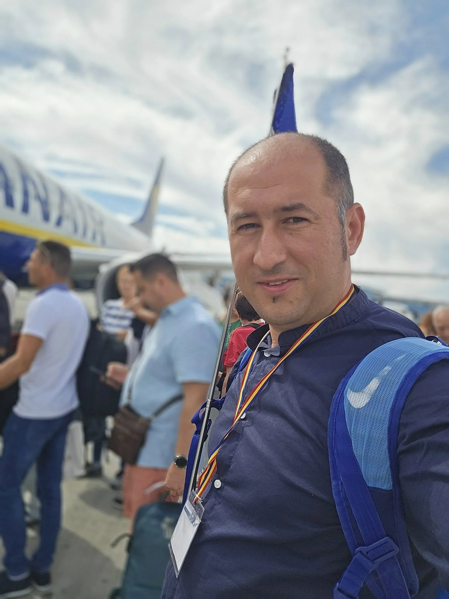 Man at airport with Ryanair airplane in background, wearing a blue shirt and carrying a blue backpack.