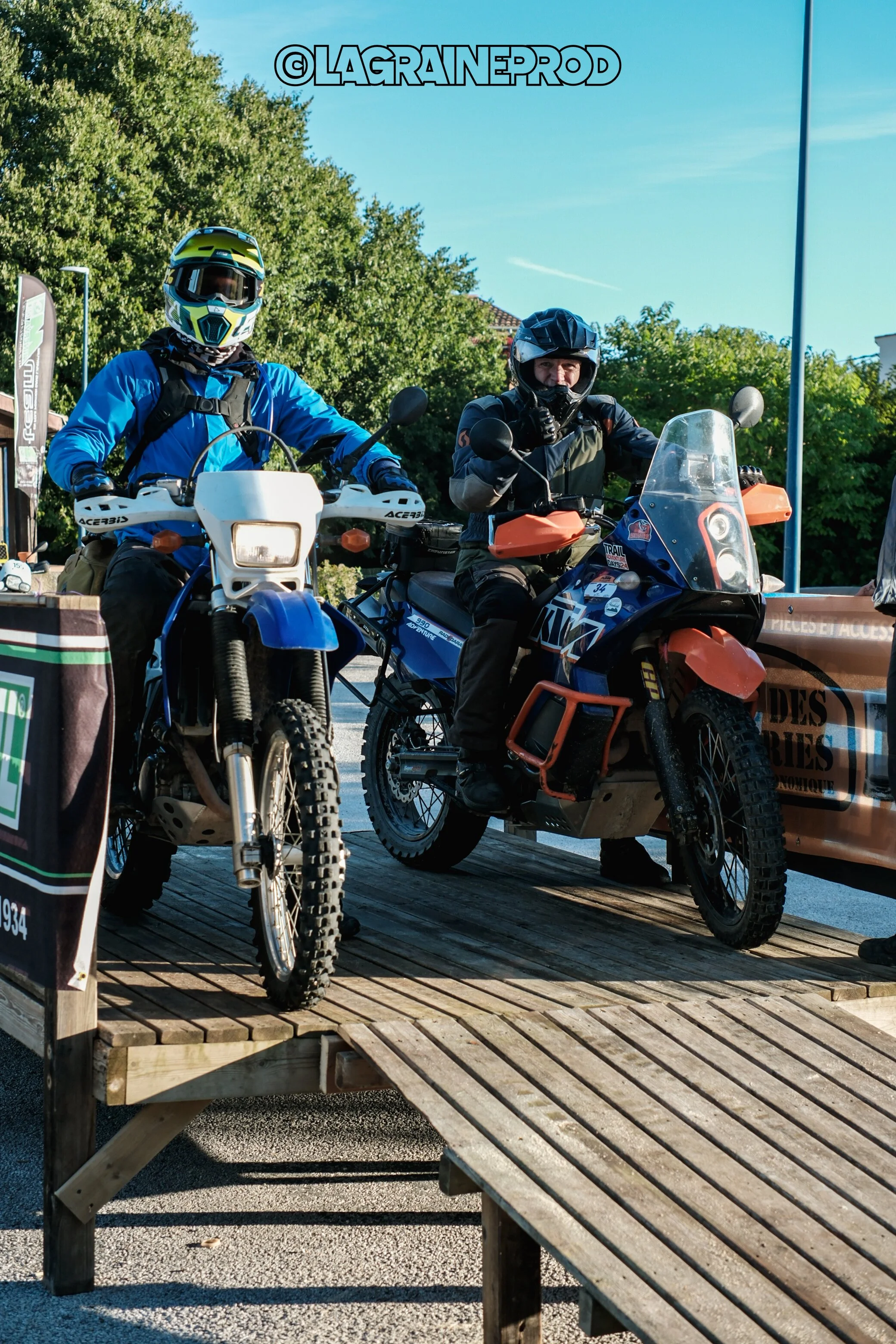 Deux motards en équipement de protection, assis sur leurs motos tout terrain, lors d'un événement en plein air.