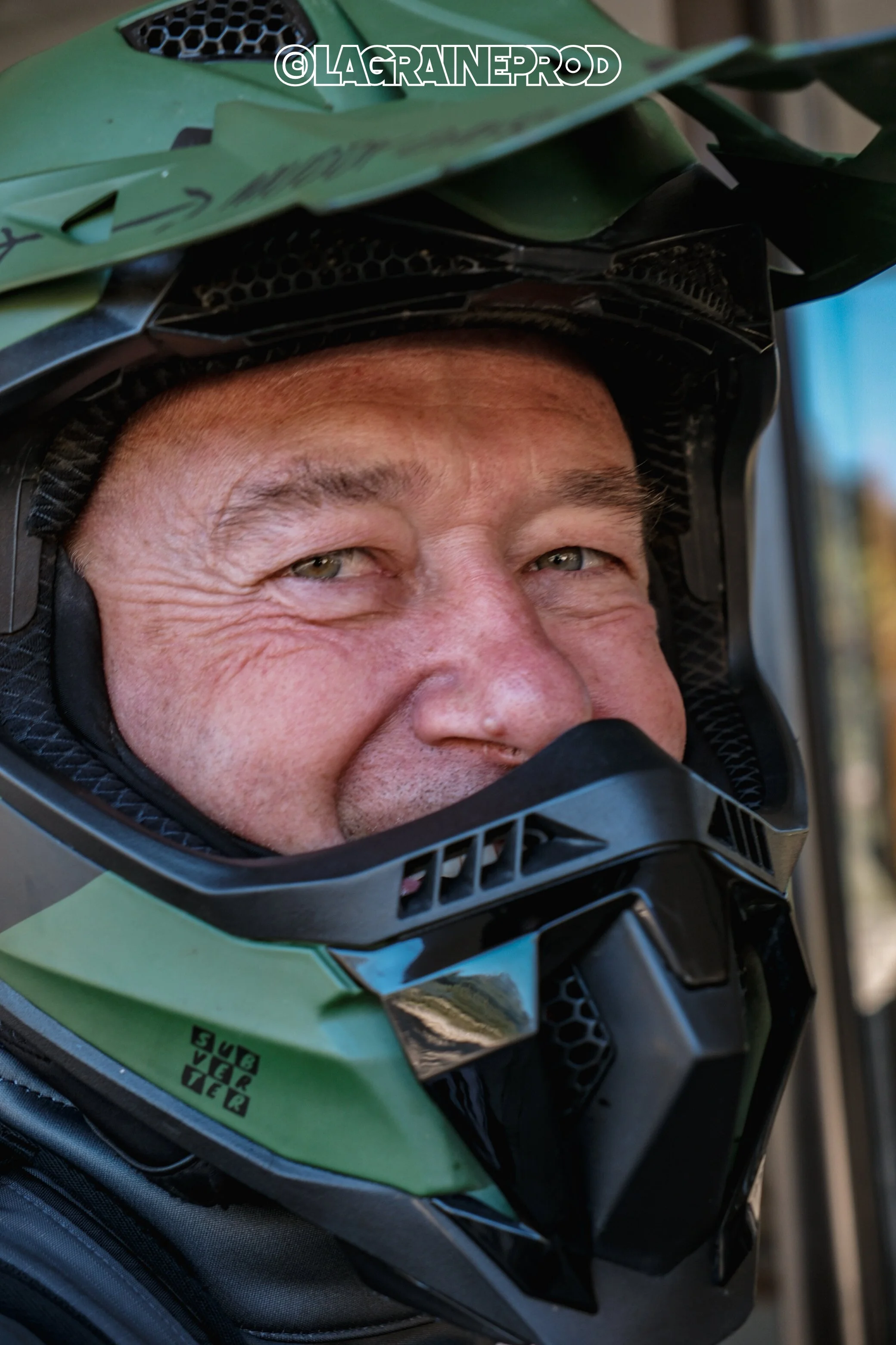 Un homme souriant porte un casque de motocross vert et noir.