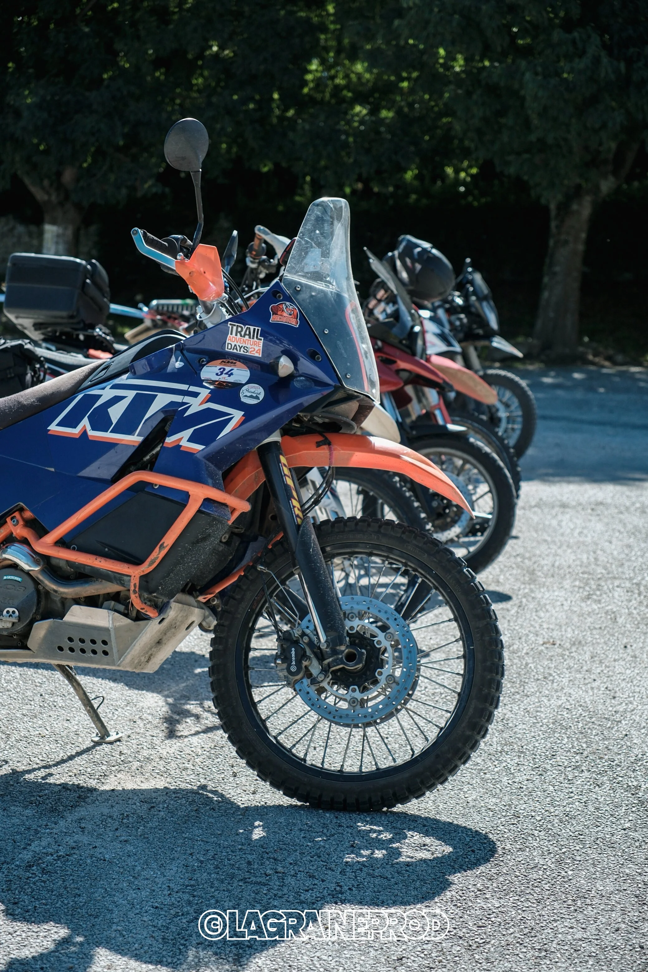 Une rangée de motos tout-terrain garées sur une surface pavée, avec des arbres en arrière-plan.