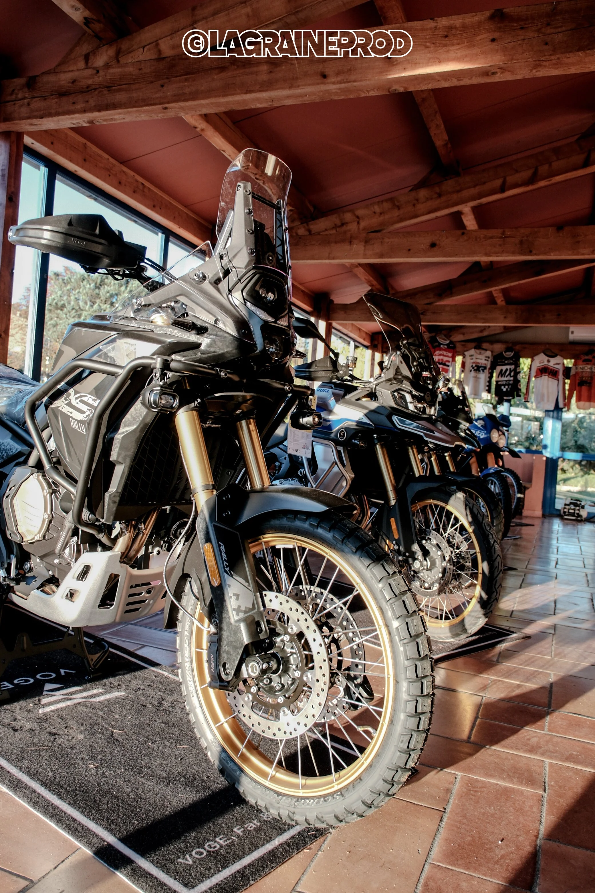Une exposition de motos tout-terrain dans un magasin, avec plusieurs modèles alignés, montrant des pneus robustes et des suspensions hautes.