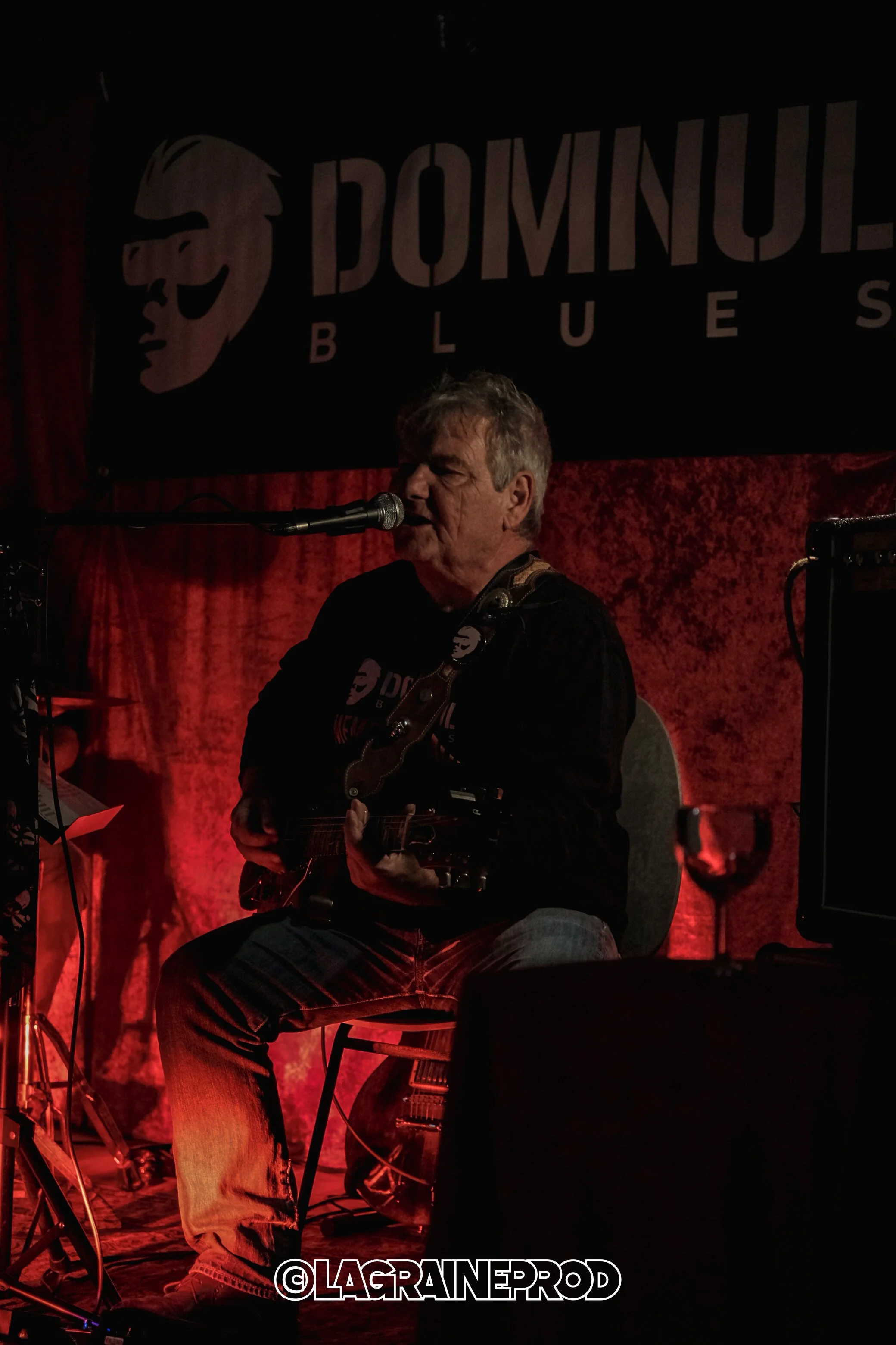 Un homme joue de la guitare et chante lors d'un concert dans une salle intitulée « Domnul Blues »