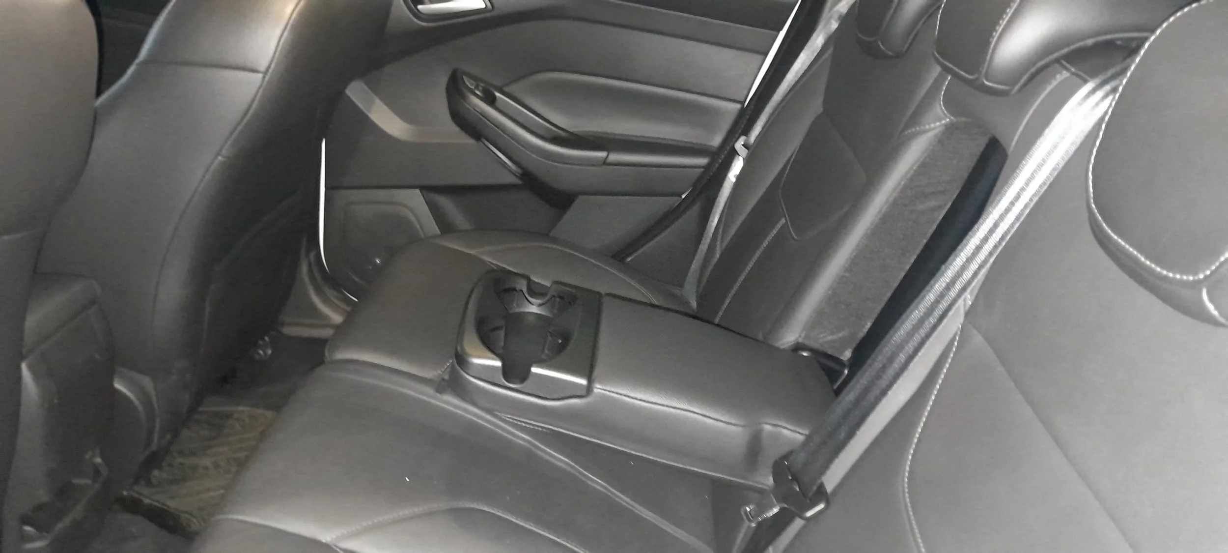 Asiento trasero de un vehículo con tapizado de cuero oscuro y un apoyabrazos con portavasos en el centro.