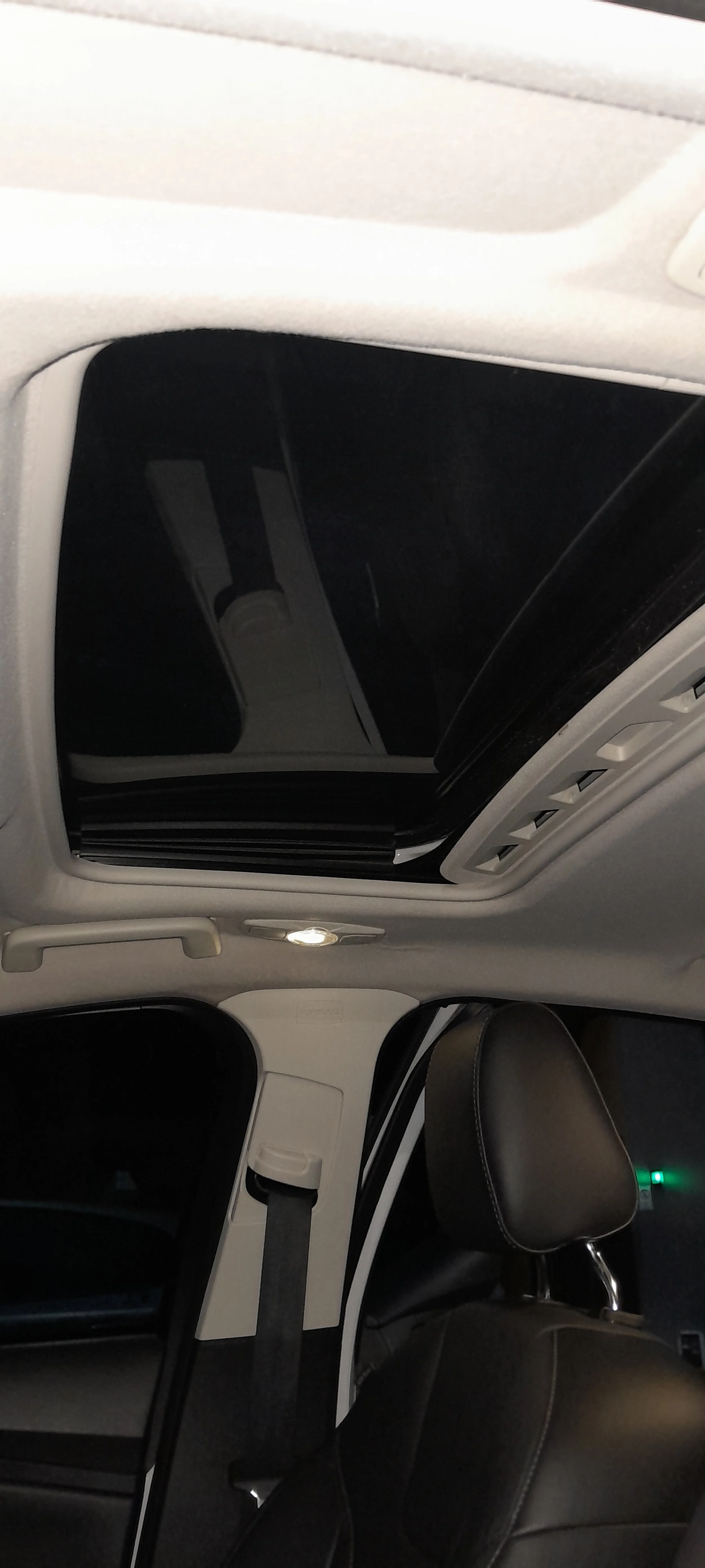 Interior de un vehículo, vista del techo con un sunroof abierto, luz interior encendida, asiento de cuero y cinturón de seguridad.