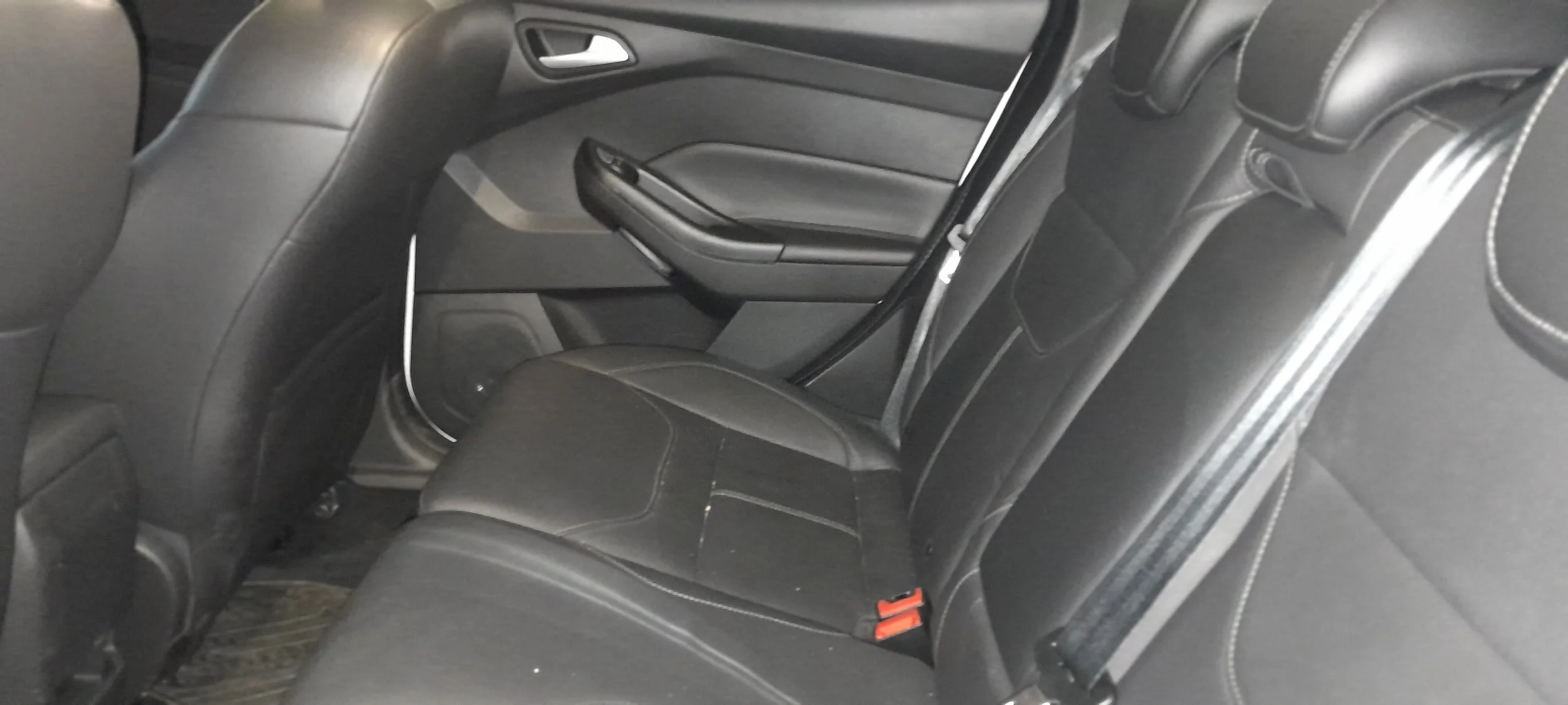 Asiento trasero de un coche con tapicería de cuero negro, cinturón de seguridad y detalles en color blanco.