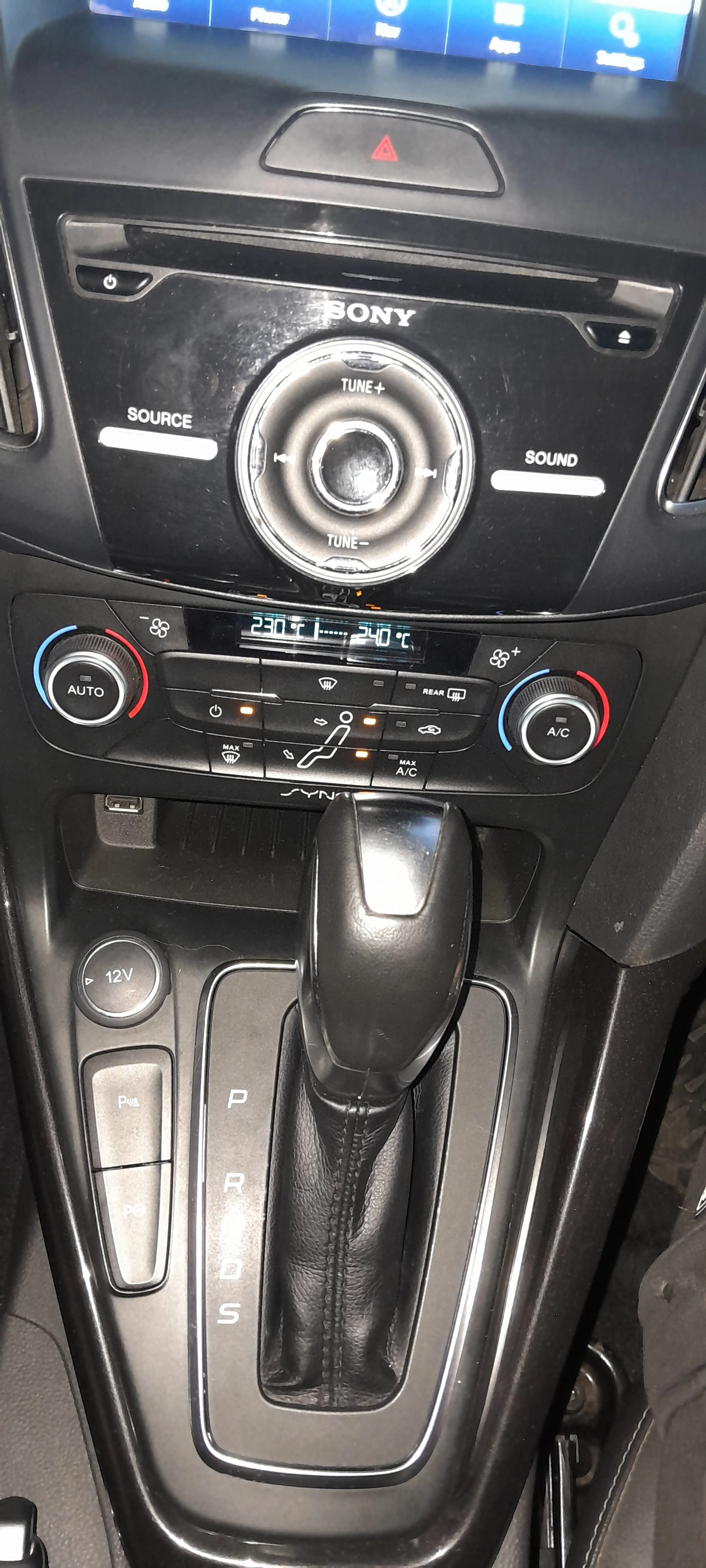 Interior de coche, consola central, transmisión automática, controles de clima y radio con pantalla digital.