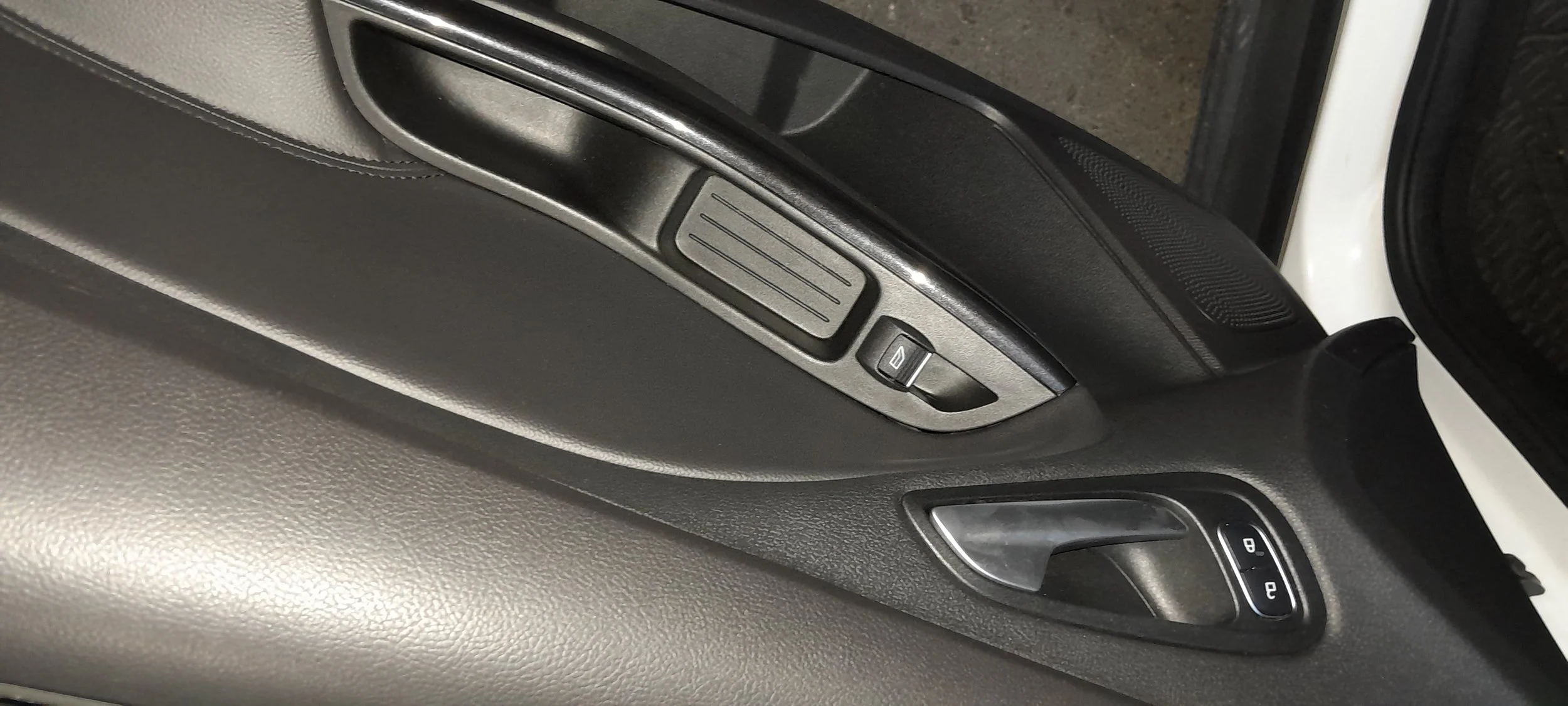 Detalles de la puerta interior de un automóvil, incluyendo el panel de control para las ventanas y la cerradura.