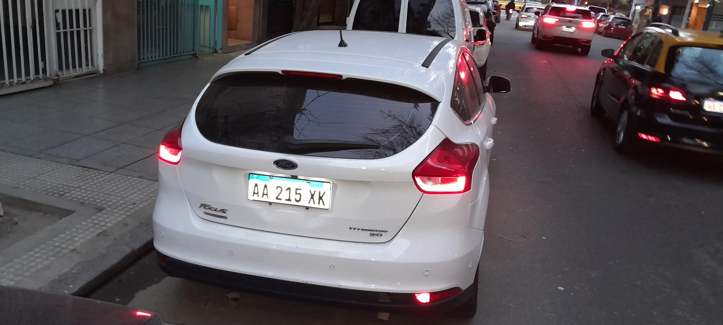 Auto Ford Focus blanco estacionado en la calle, con otras autos circulando en la calle.