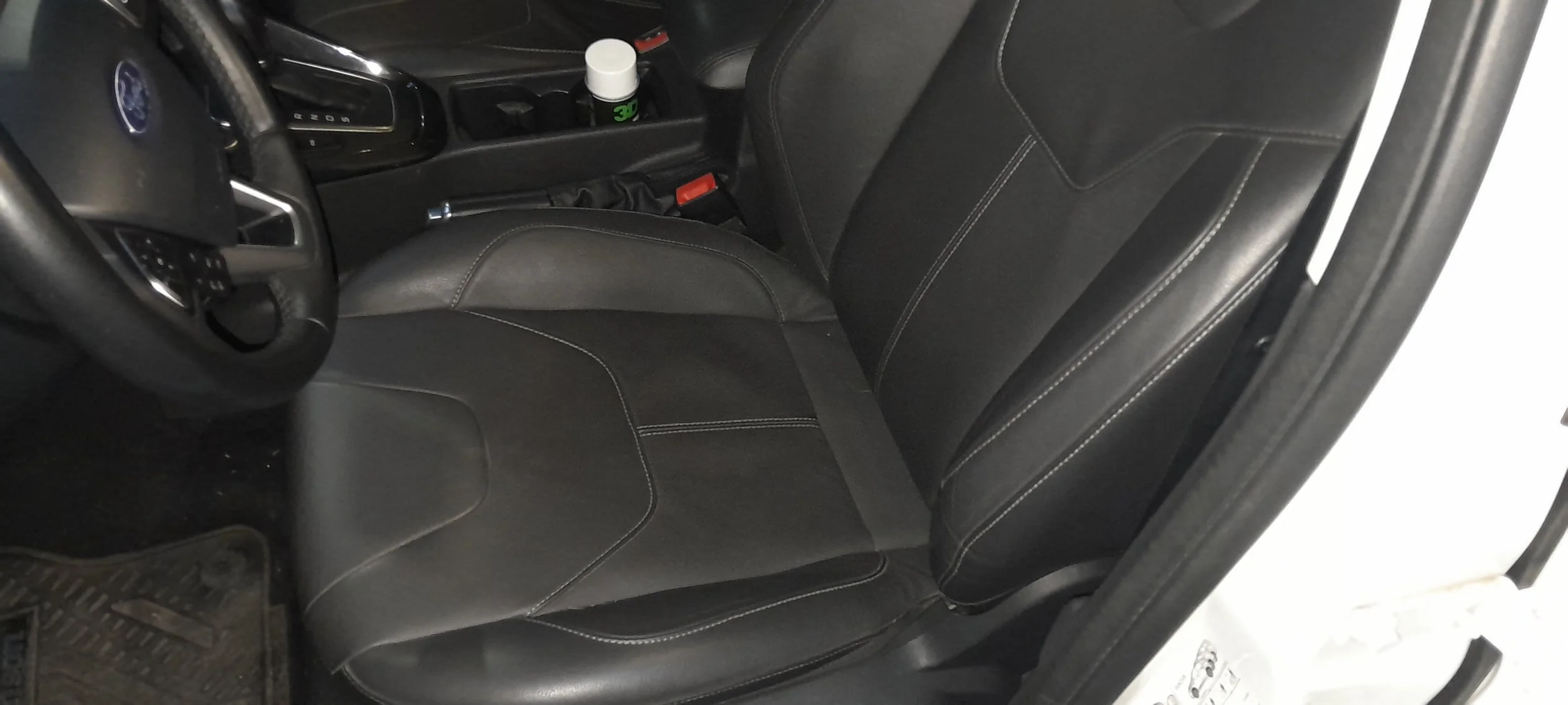 Asiento de conductor y tablero de un automóvil con controles y un envase de líquido en la consola central.