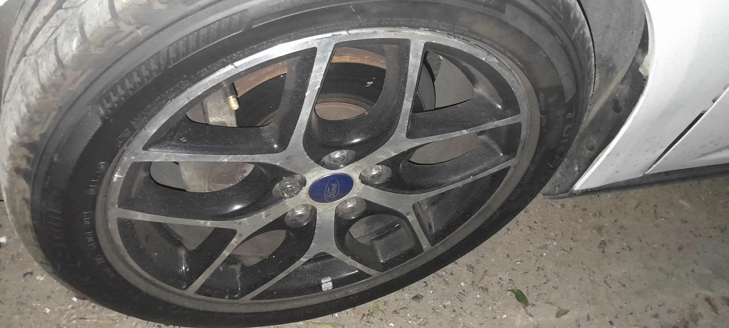 Rueda de automóvil con neumático y llanta de diseño ford, con el centro marcado con logo y algunas pequeñas manchas de suciedad y polvo.