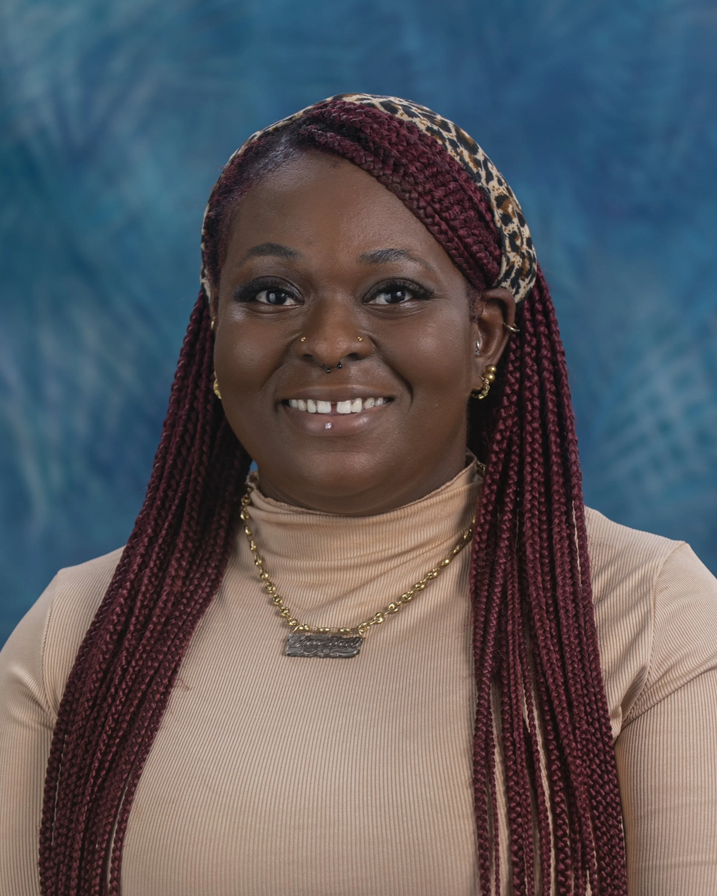 A woman with long, wavy purple hair smiling and posing in a festive sweater with holiday patterns, light blue jeans, and standing against a plain white background.
