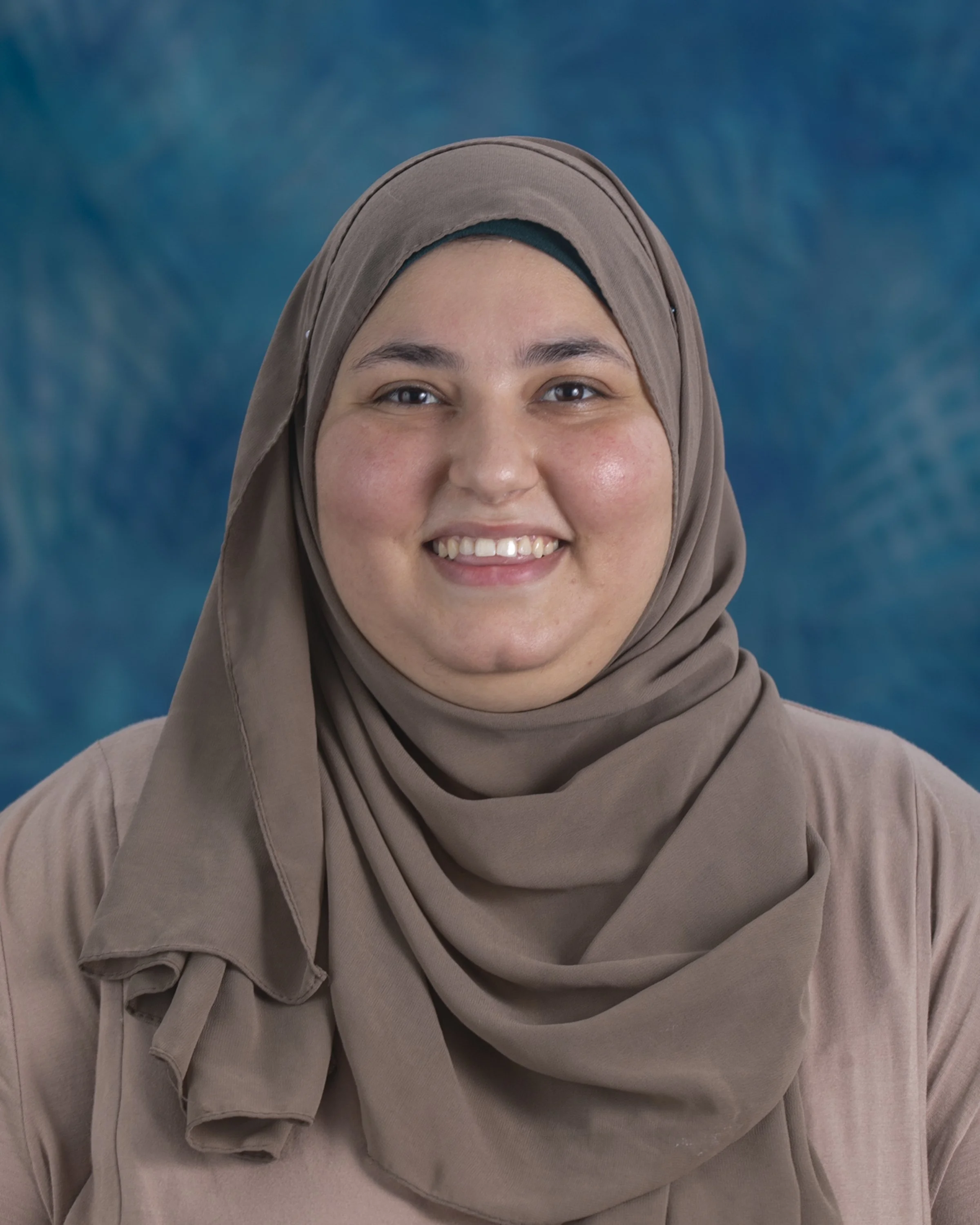 Smiling woman wearing a green hijab in a bright indoor setting.