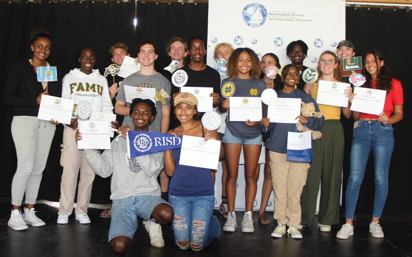 Group of students on stage holding certificates and plaques, smiling at the camera, with a banner and logo for the Rios Island Montessori School and International Academy in the background.