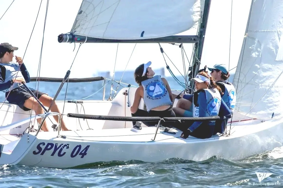 A group of young people sailing on a boat on the water, wearing life jackets and sailing gear.